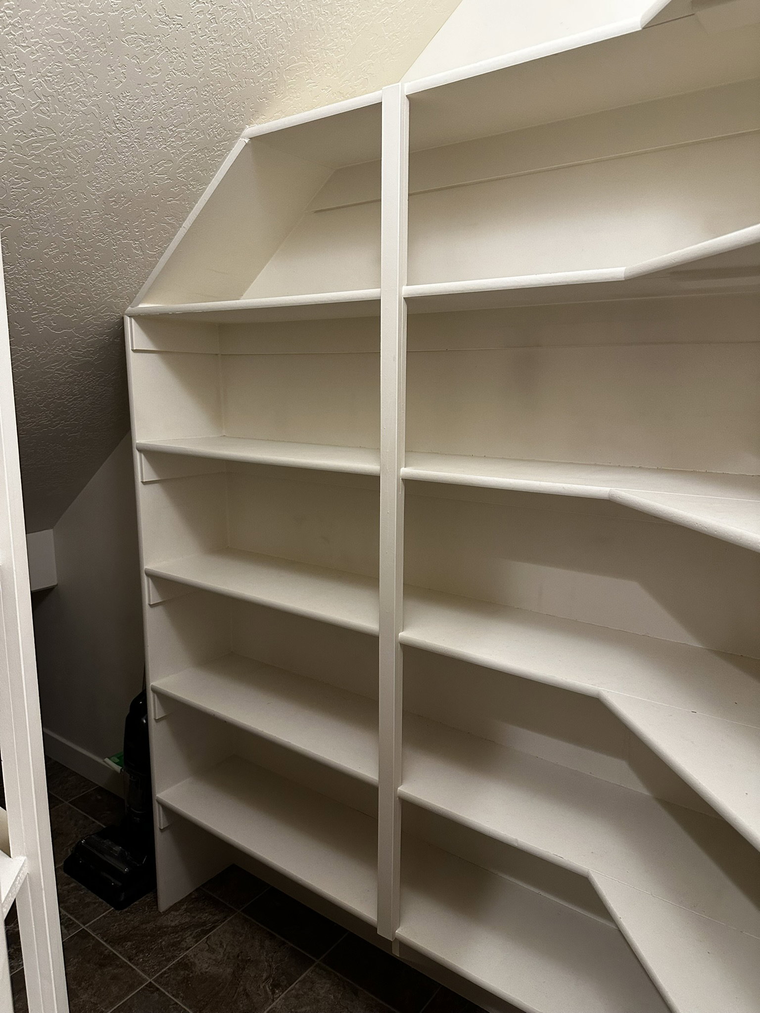 Custom built-in shelving with multiple levels, white finish, and a corner design, set against textured walls and wood-finish flooring
