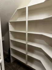 Custom built-in shelving with multiple levels, white finish, and a corner design, set against textured walls and wood-finish flooring
