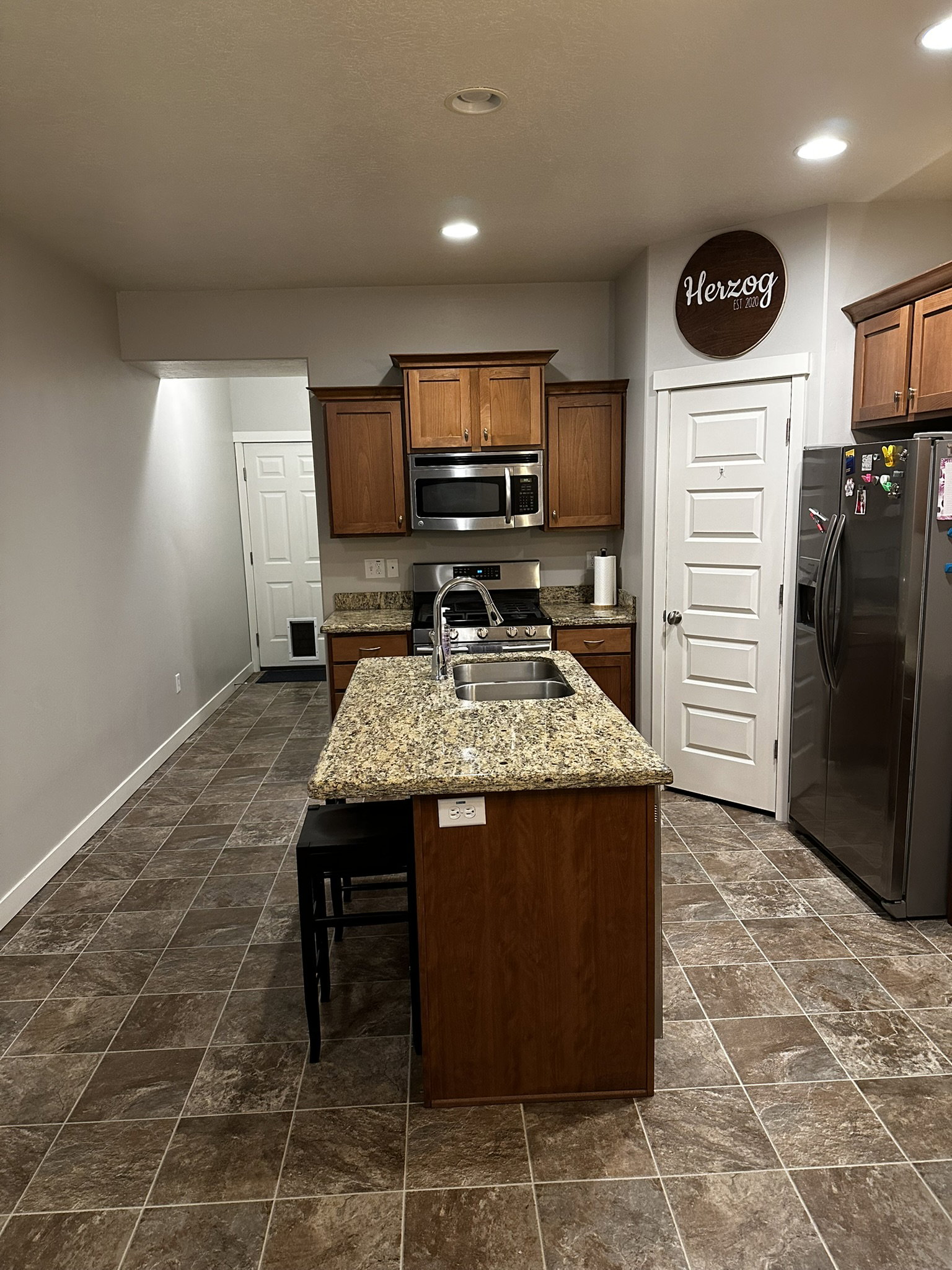 Kitchen featuring an island with a double basin sink, granite-style countertop, and recessed lighting
