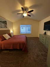 Carpeted interior space featuring a vaulted ceiling with a ceiling fan light fixture, a window with blinds, and a built-in wall-mounted television
