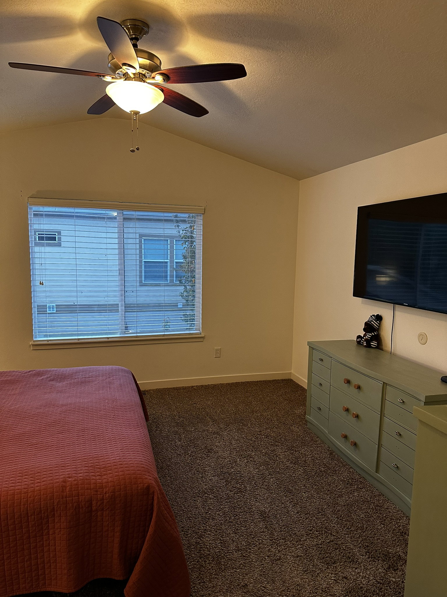Vaulted ceiling room featuring a ceiling fan with integrated lighting, a large window with blinds, and neutral-toned wall-to-wall carpeting