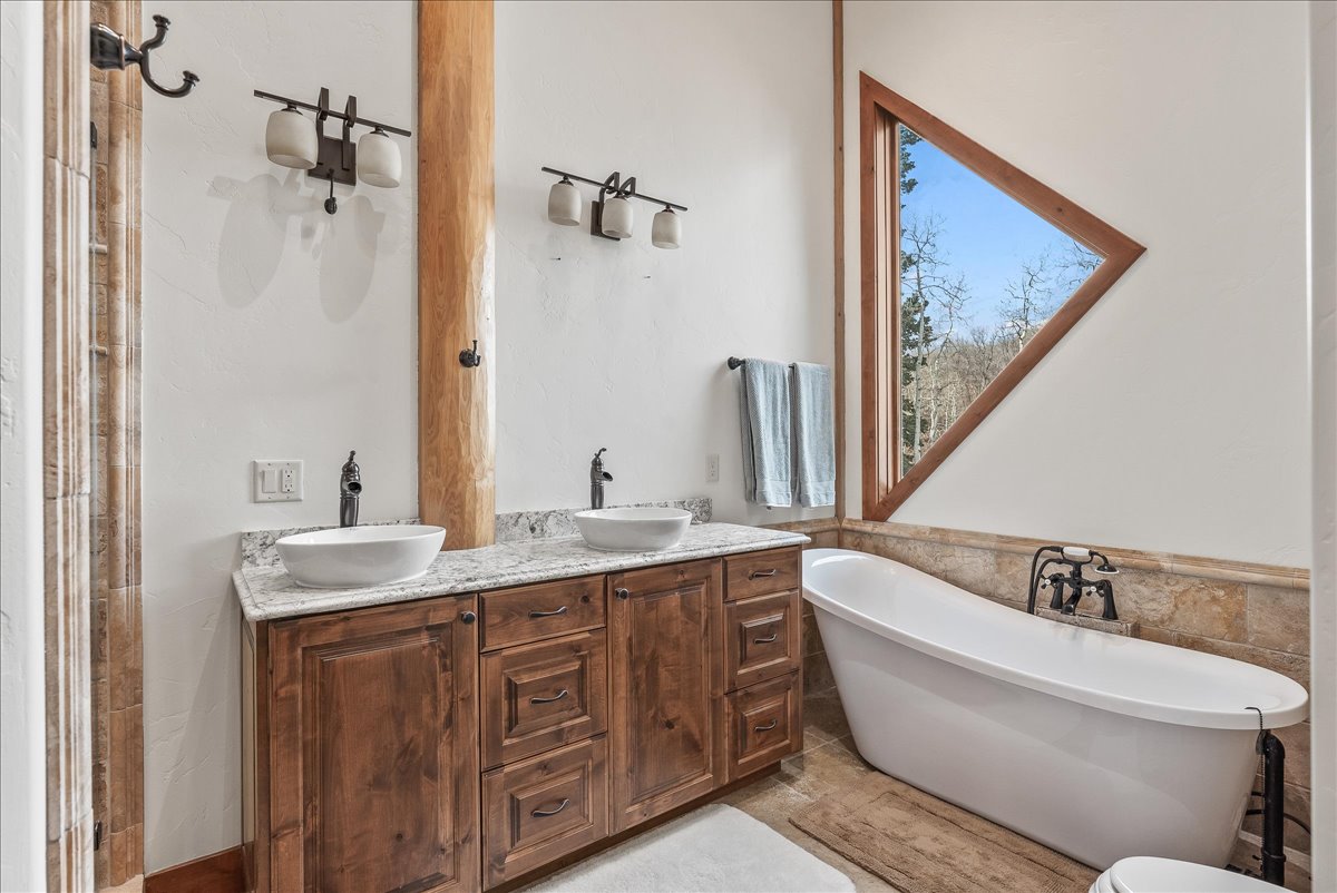 Bathroom featuring a freestanding soaking tub, a unique triangular window, and a wood-finish double vanity with vessel sinks