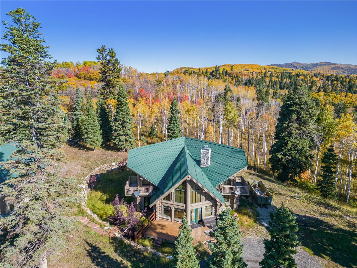 Log-style home with a distinct green metal roof, multiple decks, and a prominent stone chimney