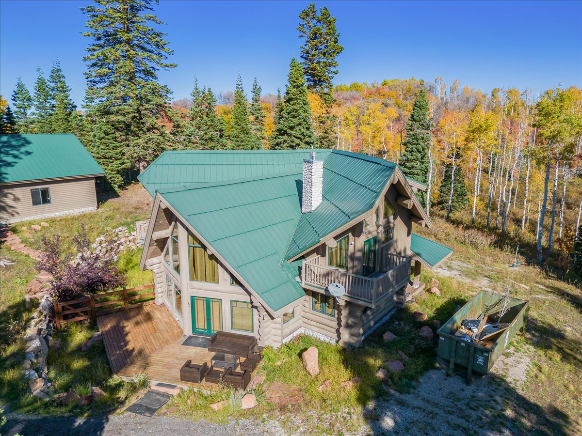 Log-sided home featuring a green metal roof and a prominent stone chimney