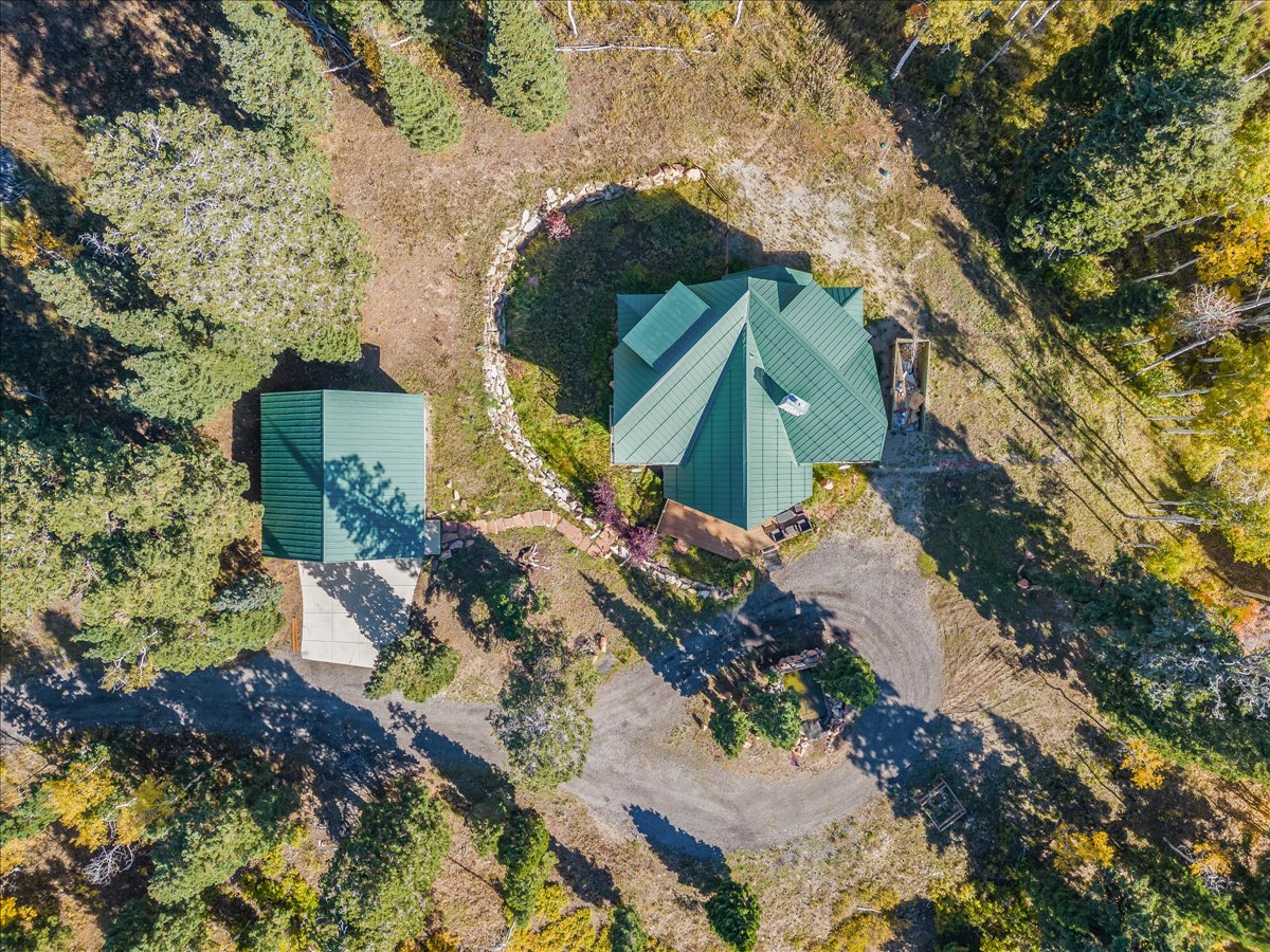 Main residence with a green metal roof, a detached structure with a matching green metal roof, a gravel driveway, and surrounding natural landscaping