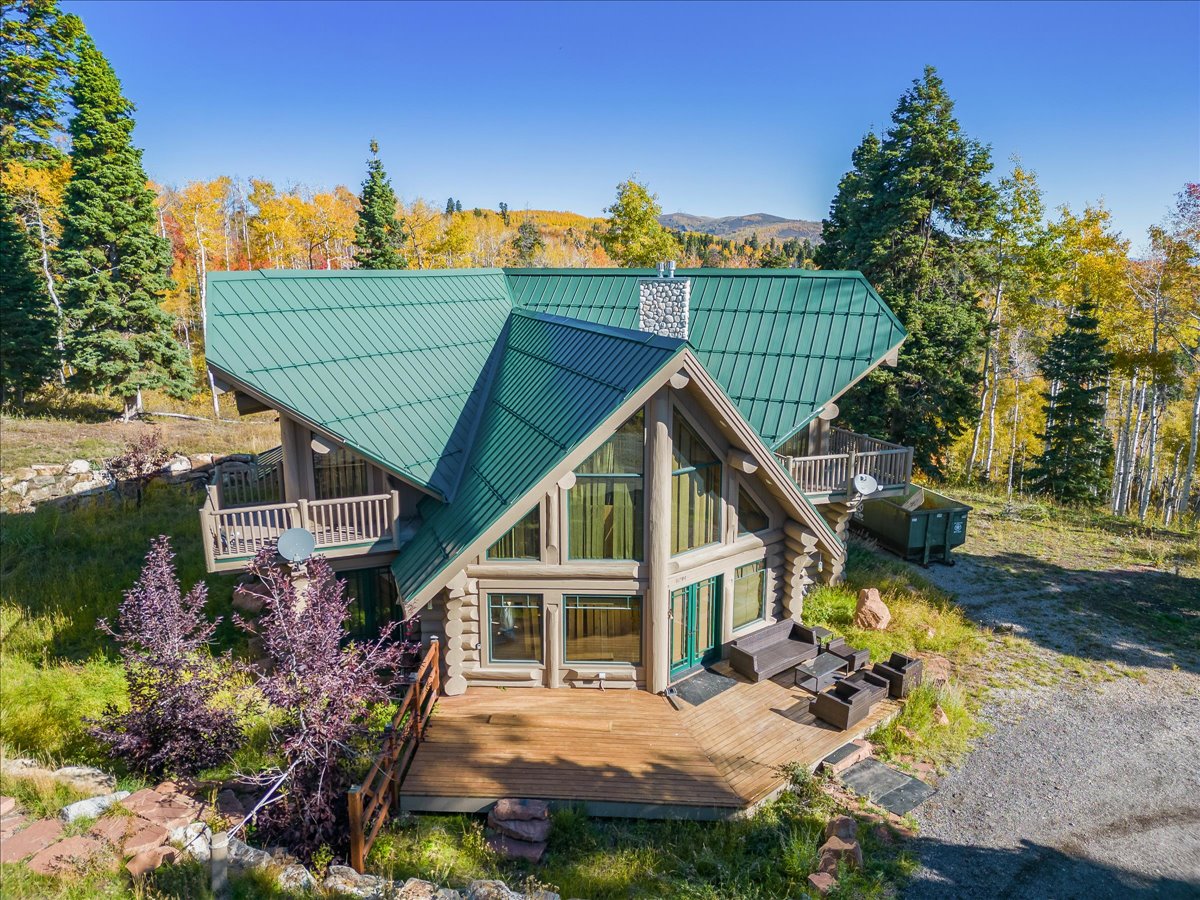 Rustic log cabin exterior featuring a green metal roof, a stone-clad chimney, and a prominent A-frame window facade