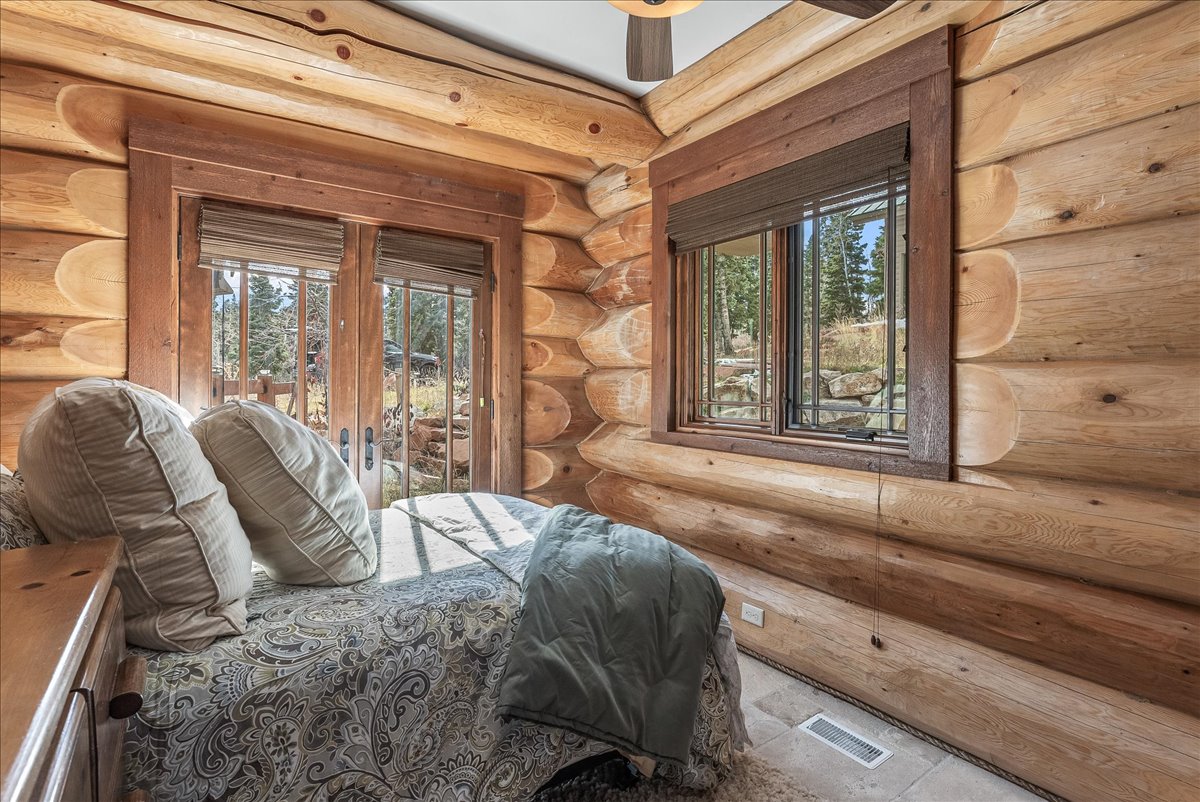 Log-style interior featuring natural wood walls, a ceiling fan, and two windows with wood blinds
