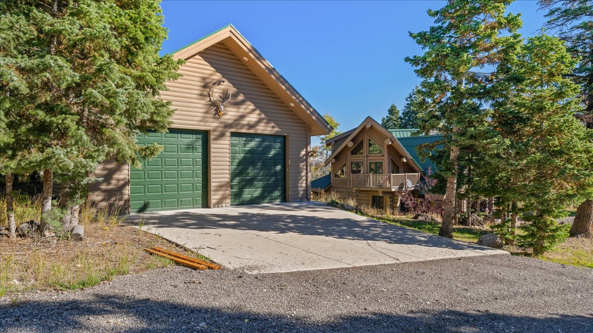 Log-sided garage with two green panel garage doors and a concrete driveway