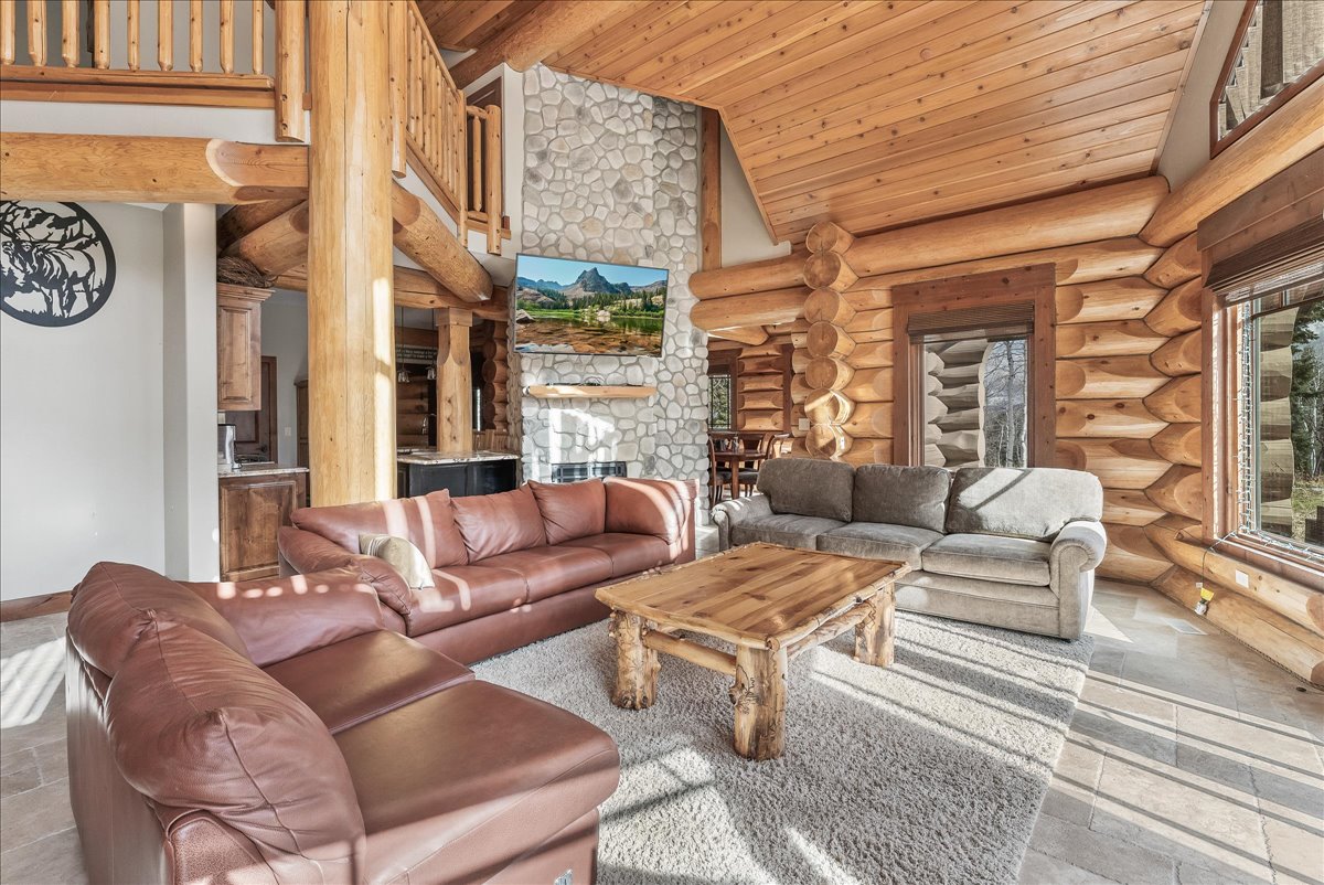 Great room featuring log construction, vaulted wood-paneled ceiling, stone fireplace, and large windows