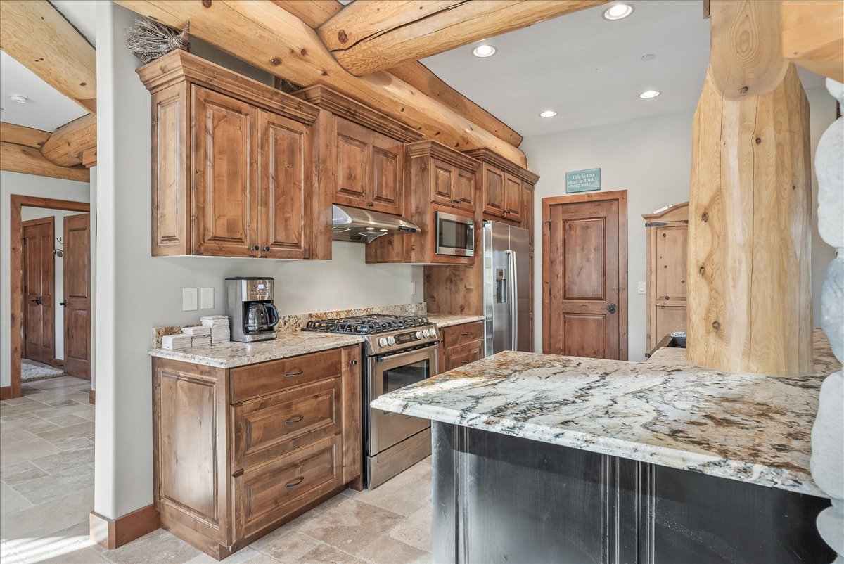 Kitchen featuring wood cabinetry, stone countertops, stainless steel appliances, recessed lighting, and wood-finish ceiling beams