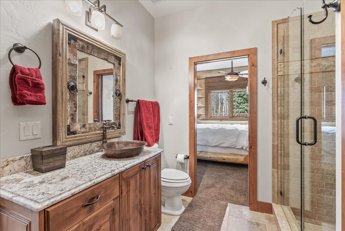 Spacious bathroom featuring a granite vanity countertop with integrated sink, wood-finish cabinetry, and a glass-enclosed shower with tiled walls