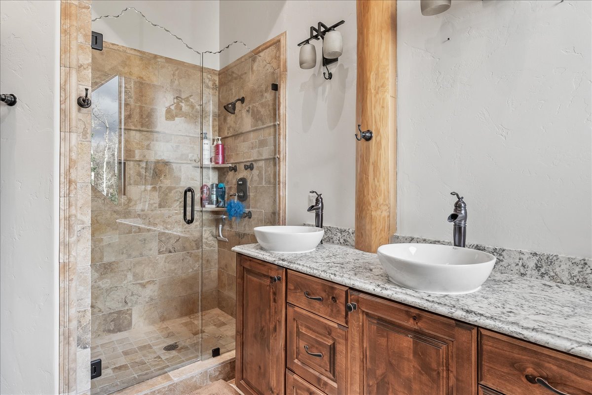 Dual vessel sinks set on a light-toned countertop with wood cabinetry