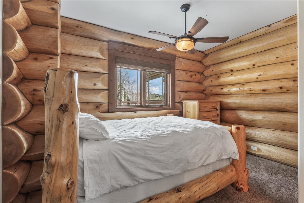 Log cabin-style room featuring natural wood walls, a wood-framed window, and a ceiling fan with integrated lighting