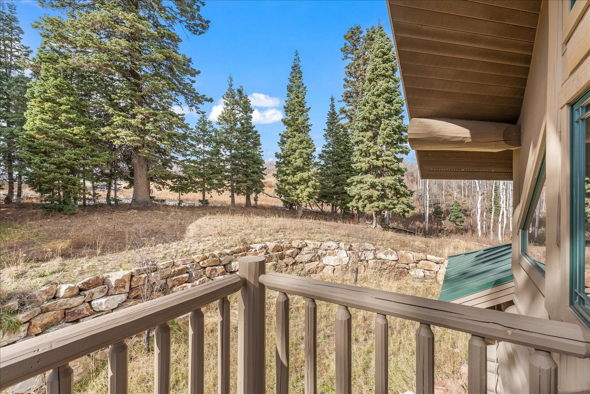 Wooden railing balcony overlooking a natural landscape with mature evergreen trees and a stone retaining wall