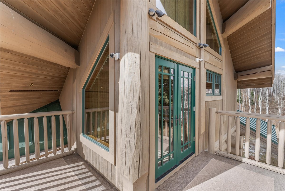 Exterior balcony featuring exposed timber framing, natural wood siding, green-framed glass doors, and a wood railing