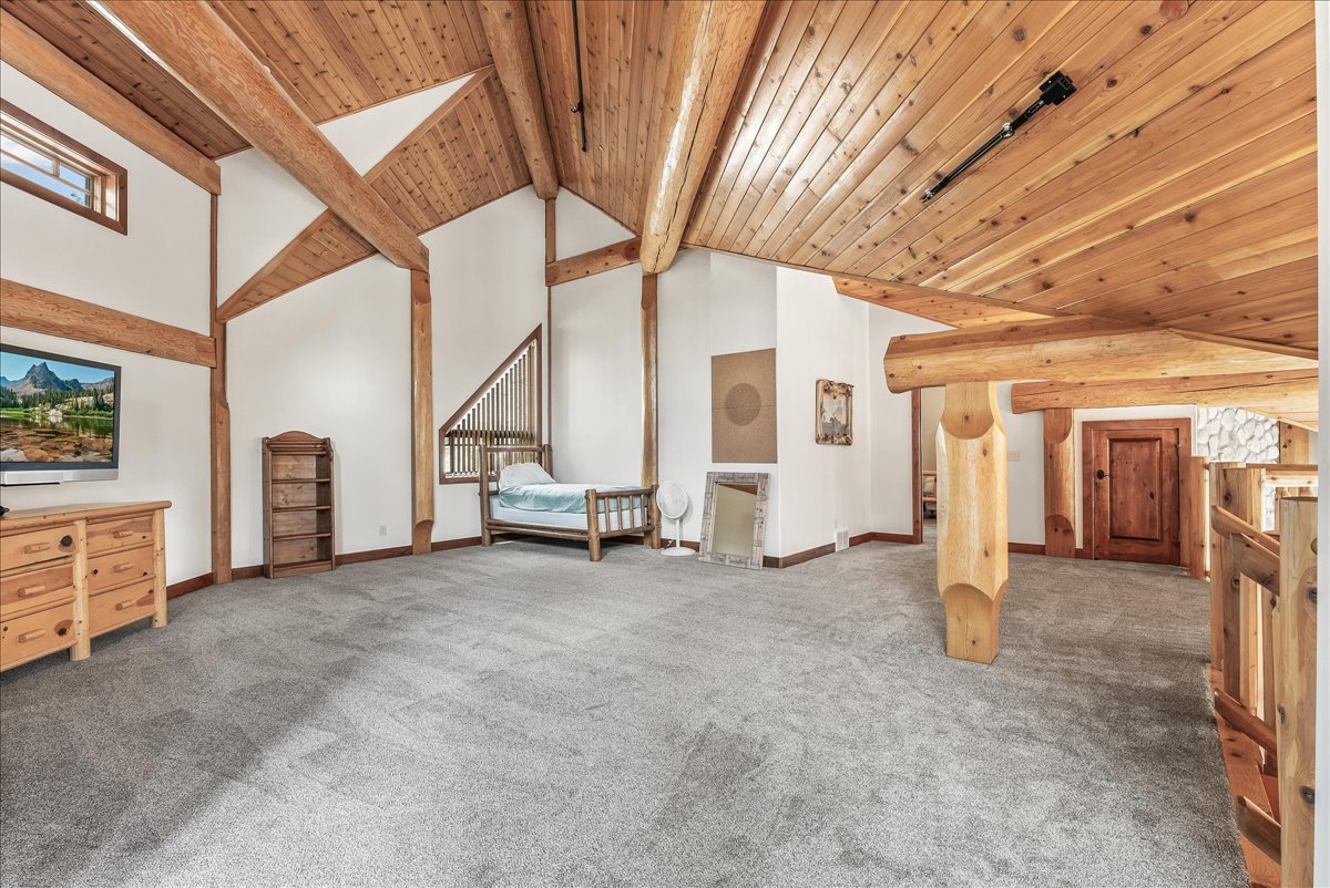 Spacious room featuring exposed wood beams, vaulted wood plank ceilings, plush gray carpeting, white walls, and a built-in wood railing