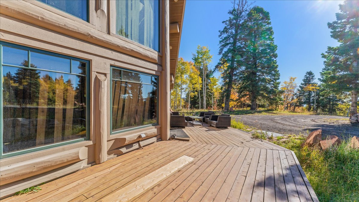 Expansive wood deck with a natural wood finish, featuring a log cabin style exterior with large windows, surrounded by mature trees