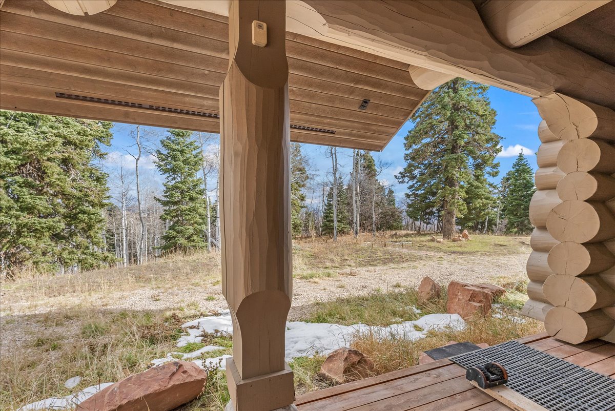 Covered porch featuring a natural wood ceiling, carved log post, and log wall construction
