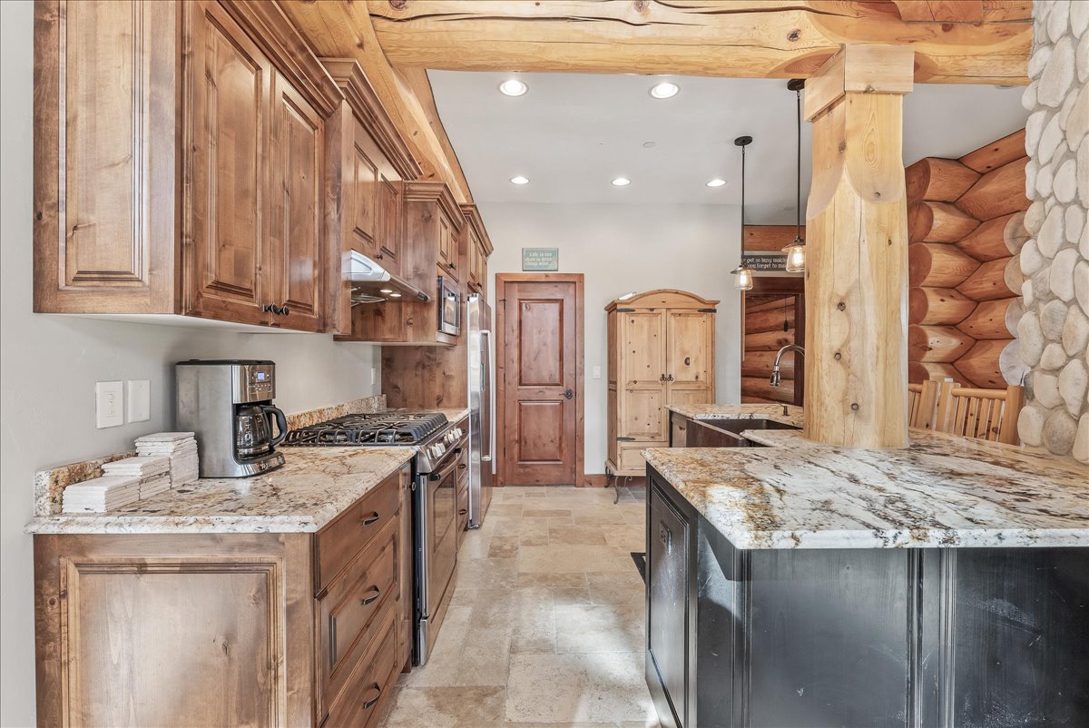 Kitchen featuring wood cabinetry, light-toned stone countertops, a gas range with a stainless steel hood, and integrated stainless steel appliances