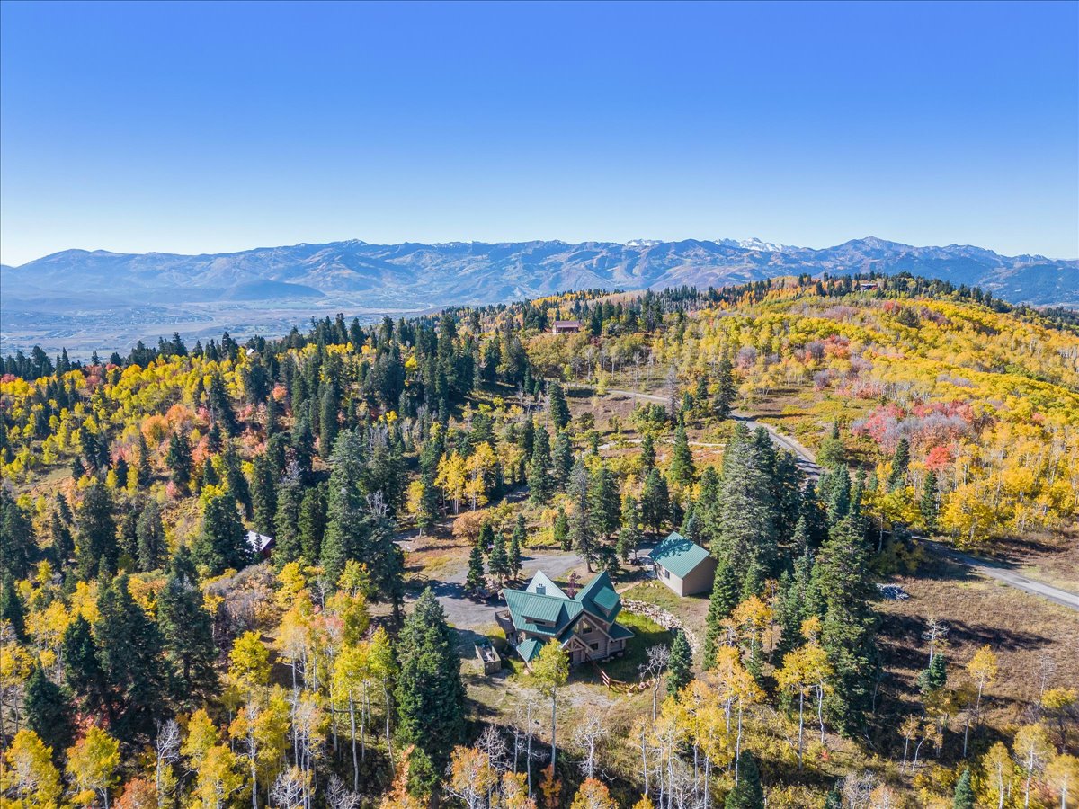 Expansive mountainous terrain featuring a residential structure and outbuildings amidst dense autumnal foliage and evergreen trees
