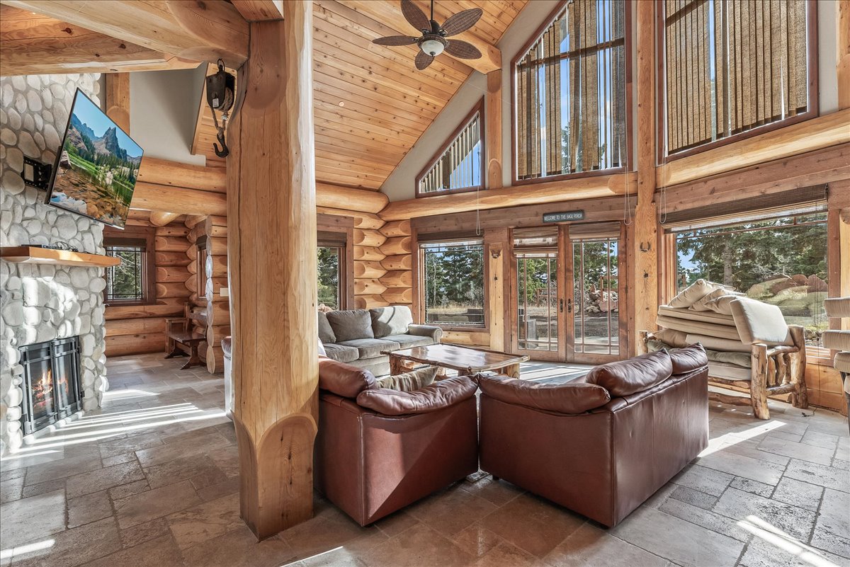 Spacious great room featuring a stone fireplace with a wood mantle, large exposed log beams, high vaulted wood ceilings, and extensive window walls