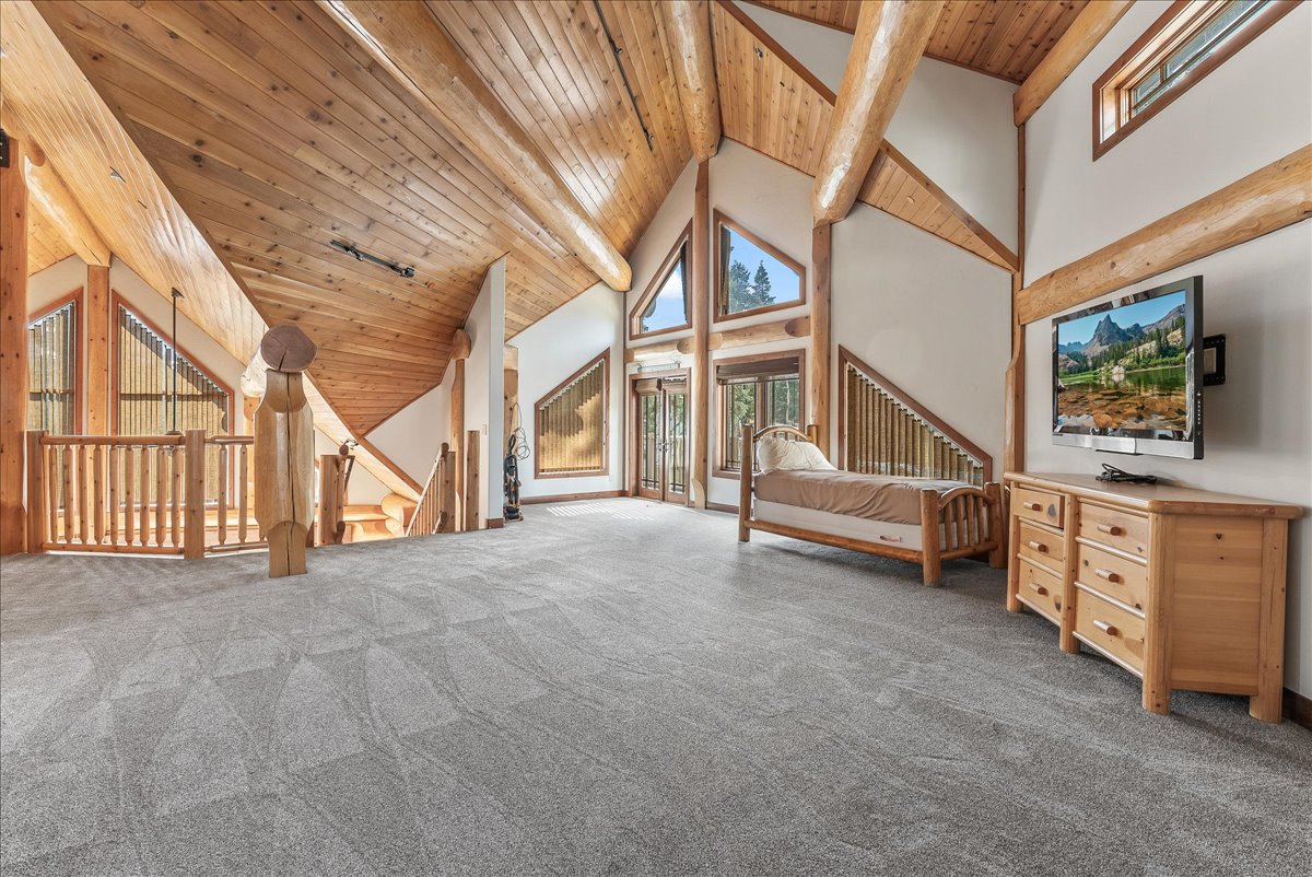 Spacious loft area featuring a vaulted wood-finish ceiling with exposed beams, light-colored carpeting, a wood-finish railing, and large windows