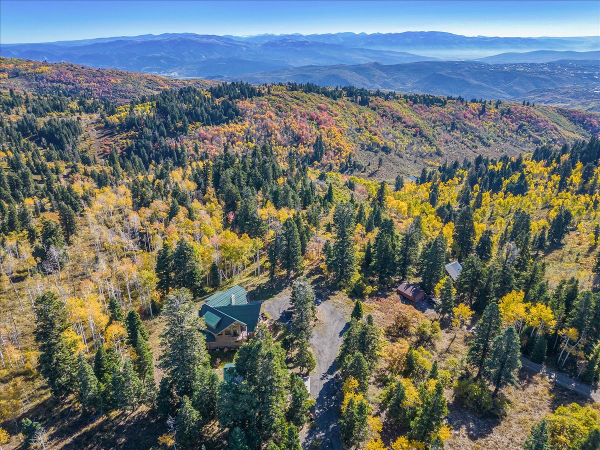 Expansive mountainous landscape featuring a single-family residence with a green roof, surrounded by mature evergreen trees and deciduous trees with autumn foliage
