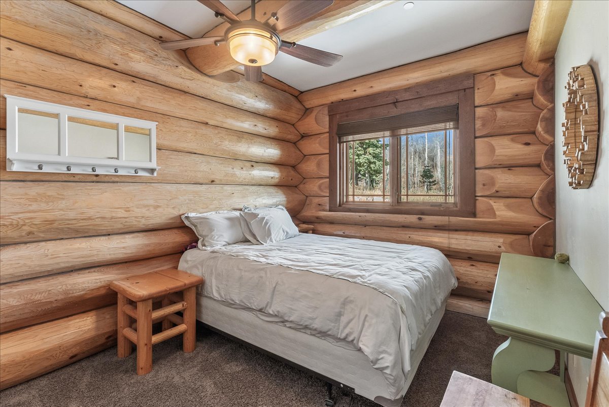 Log-cabin interior with natural wood walls, a ceiling fan with integrated lighting, a window with exterior views, and neutral carpet flooring