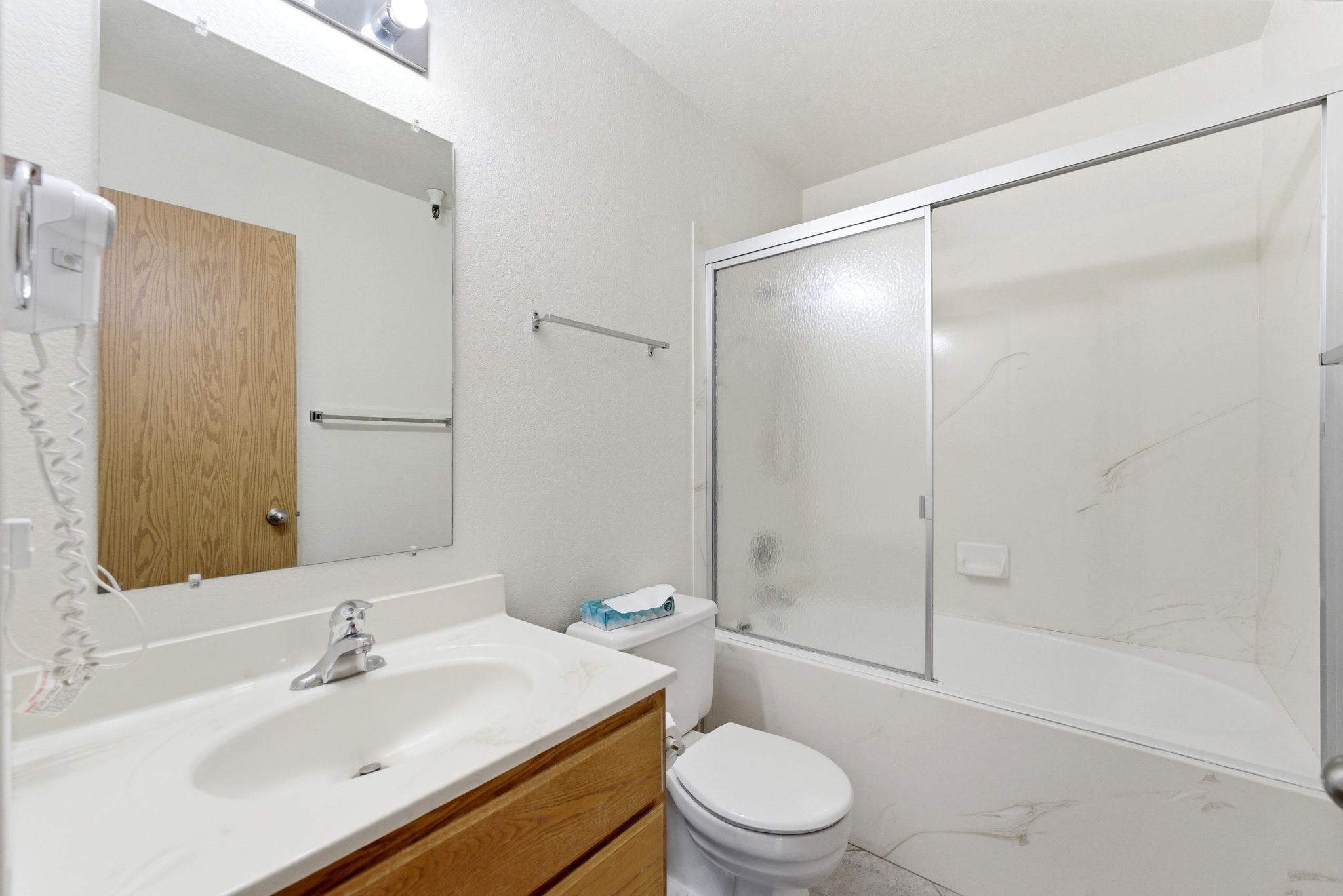 Bathroom featuring a wood-finish vanity with an integrated white sink, a chrome faucet, and a sliding glass shower door