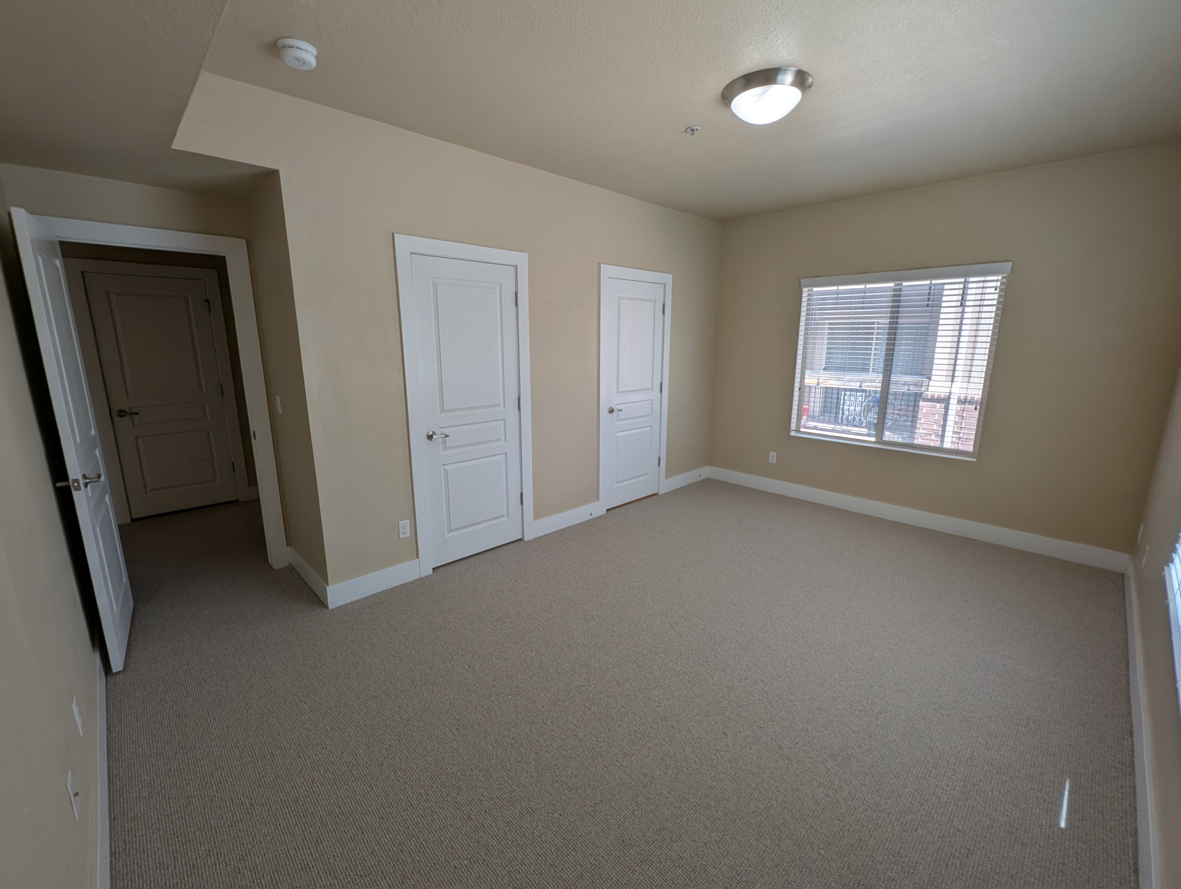Spacious room with neutral-toned carpeting, light beige walls, and white baseboards