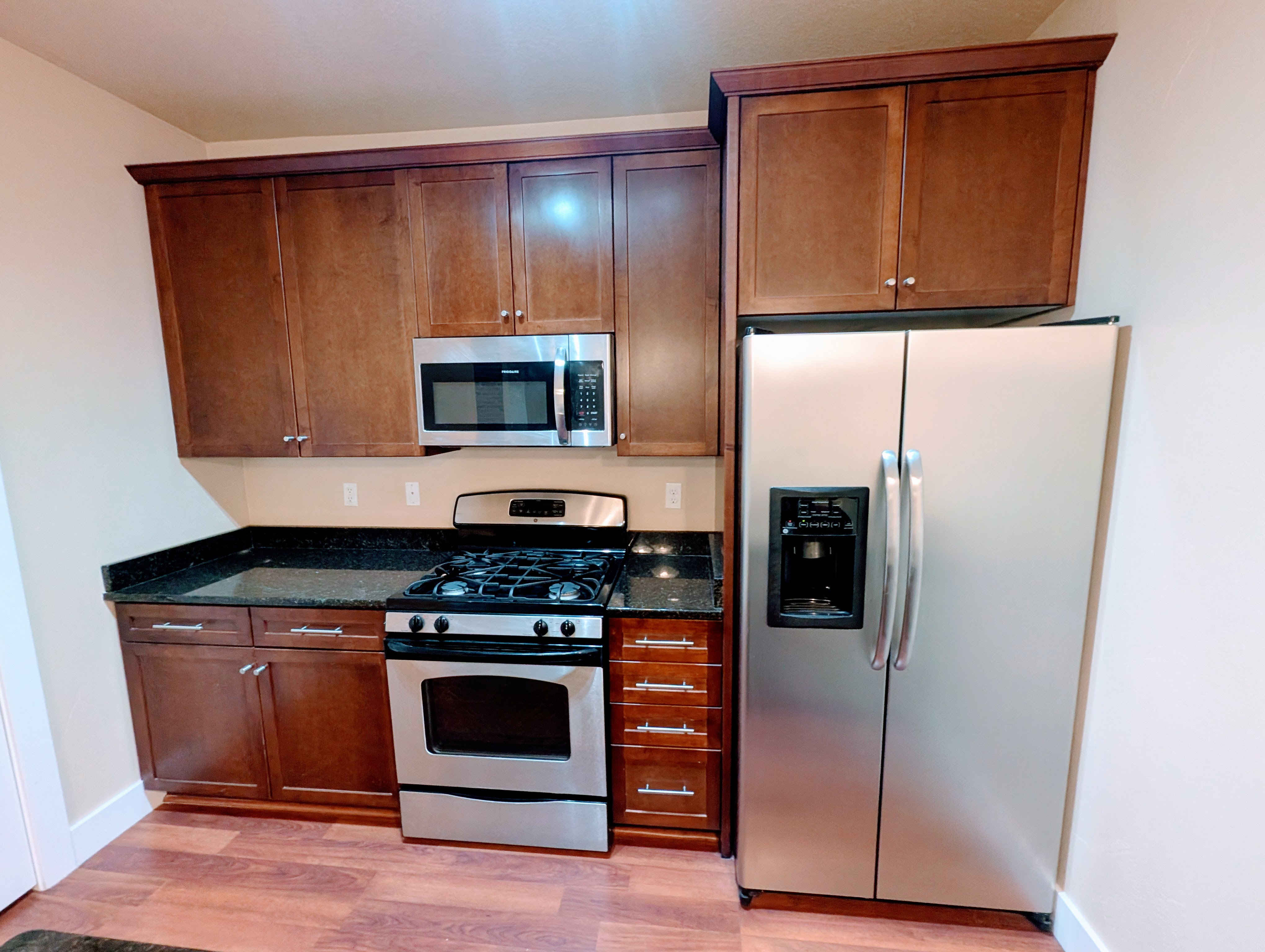 Kitchen featuring wood-finish flooring, dark wood cabinetry with crown molding, stainless steel appliances, and dark countertops