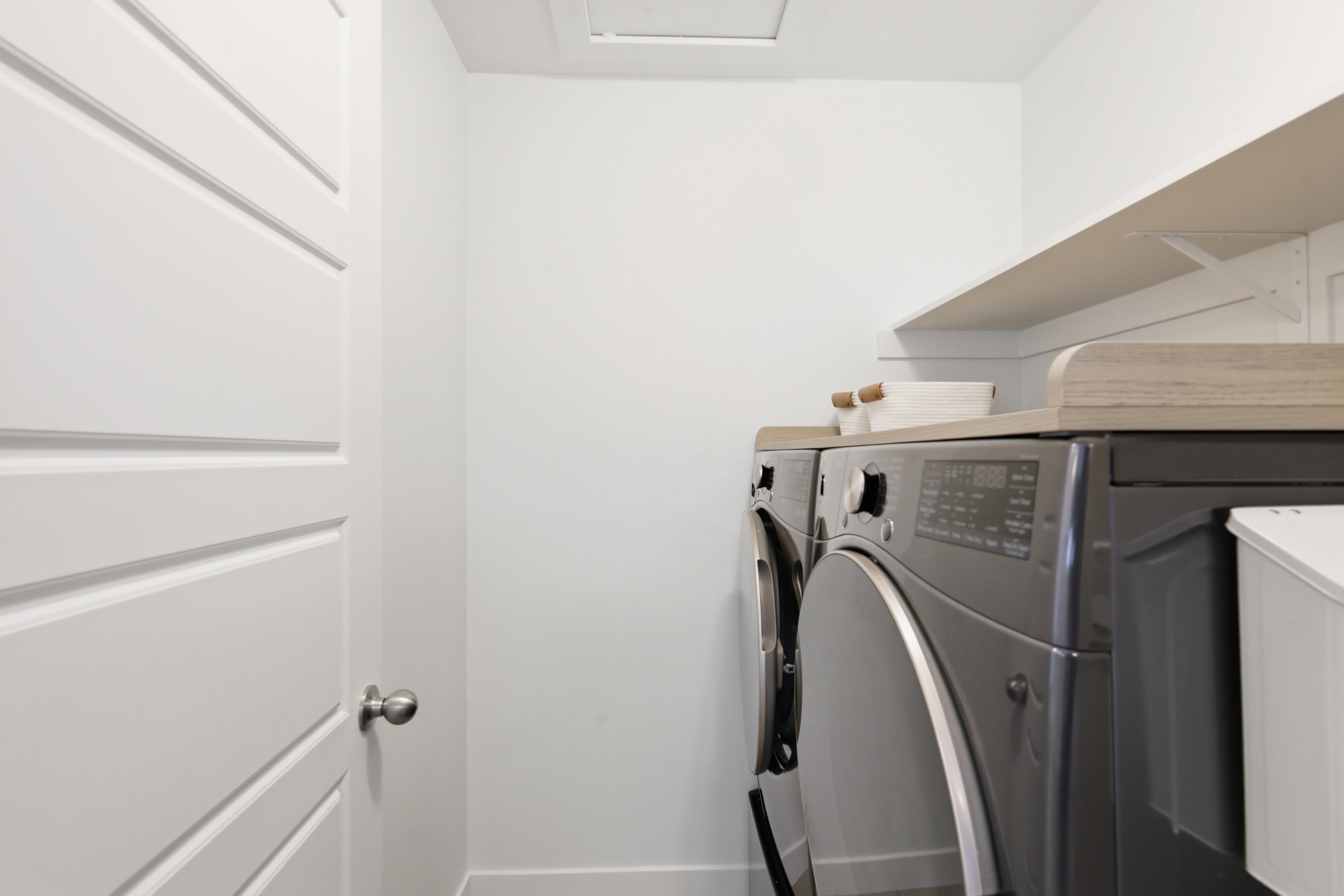 Dedicated laundry area featuring a wood-finish countertop, white shelving, and crisp white walls