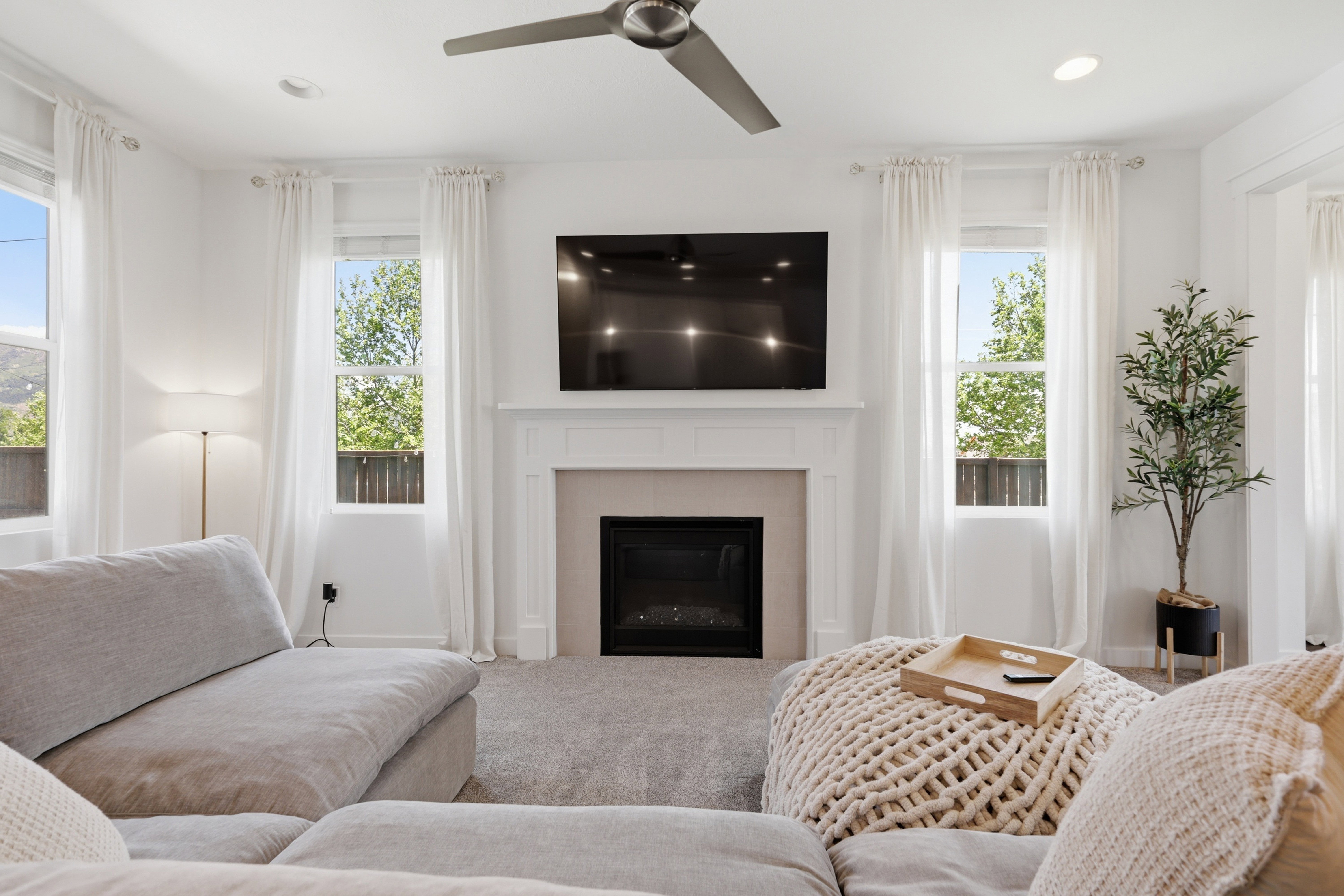 Living area featuring a central fireplace with a mantel, recessed lighting, a ceiling fan, and multiple windows