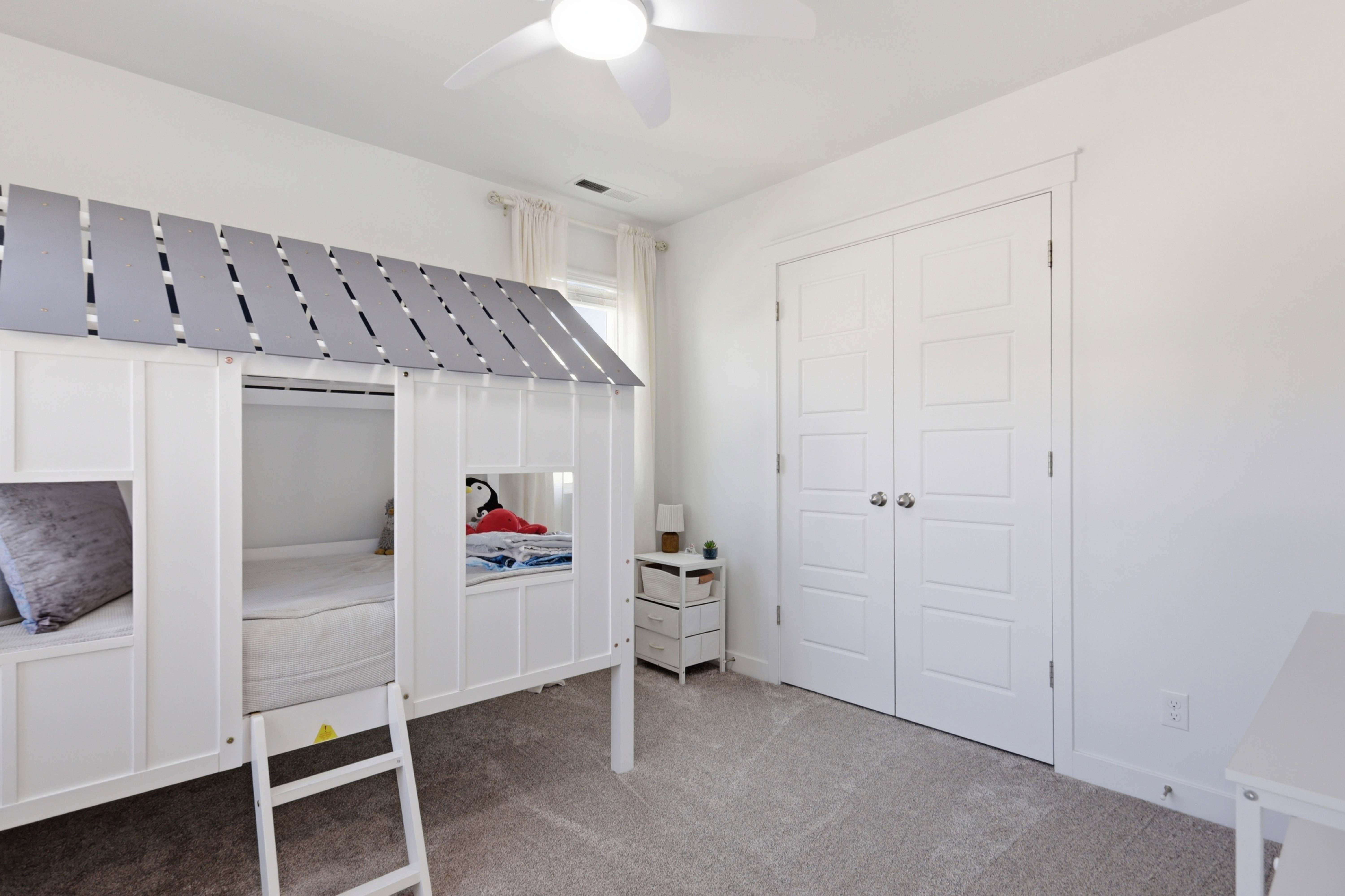 Bright room featuring plush carpet flooring, a multi-paneled double-door closet, a ceiling fan, and a window with sheer curtains