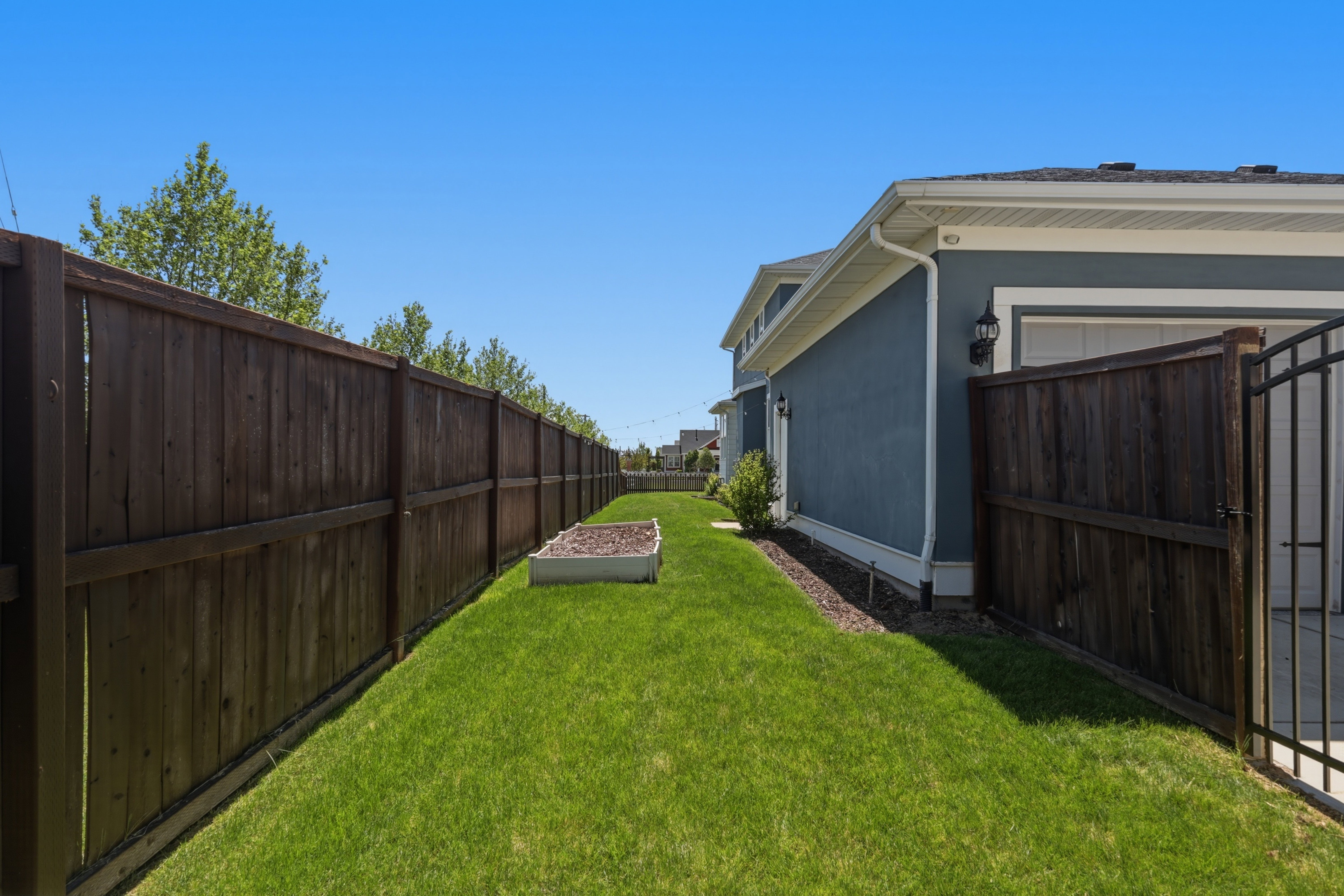 Expansive side yard featuring a privacy fence, established lawn, and raised garden bed