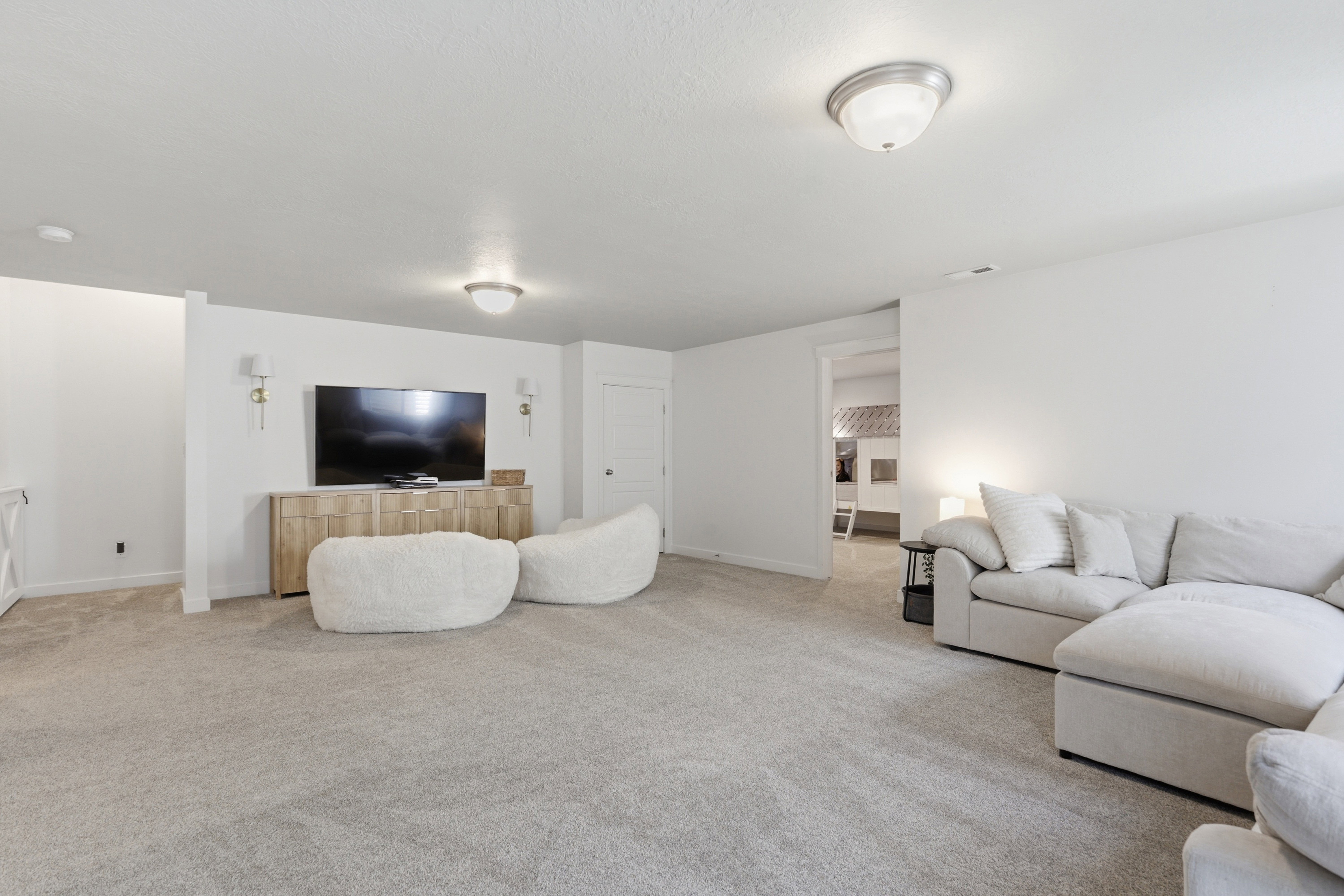 Spacious carpeted room featuring white walls, recessed ceiling lighting, and a doorway opening to an additional interior space
