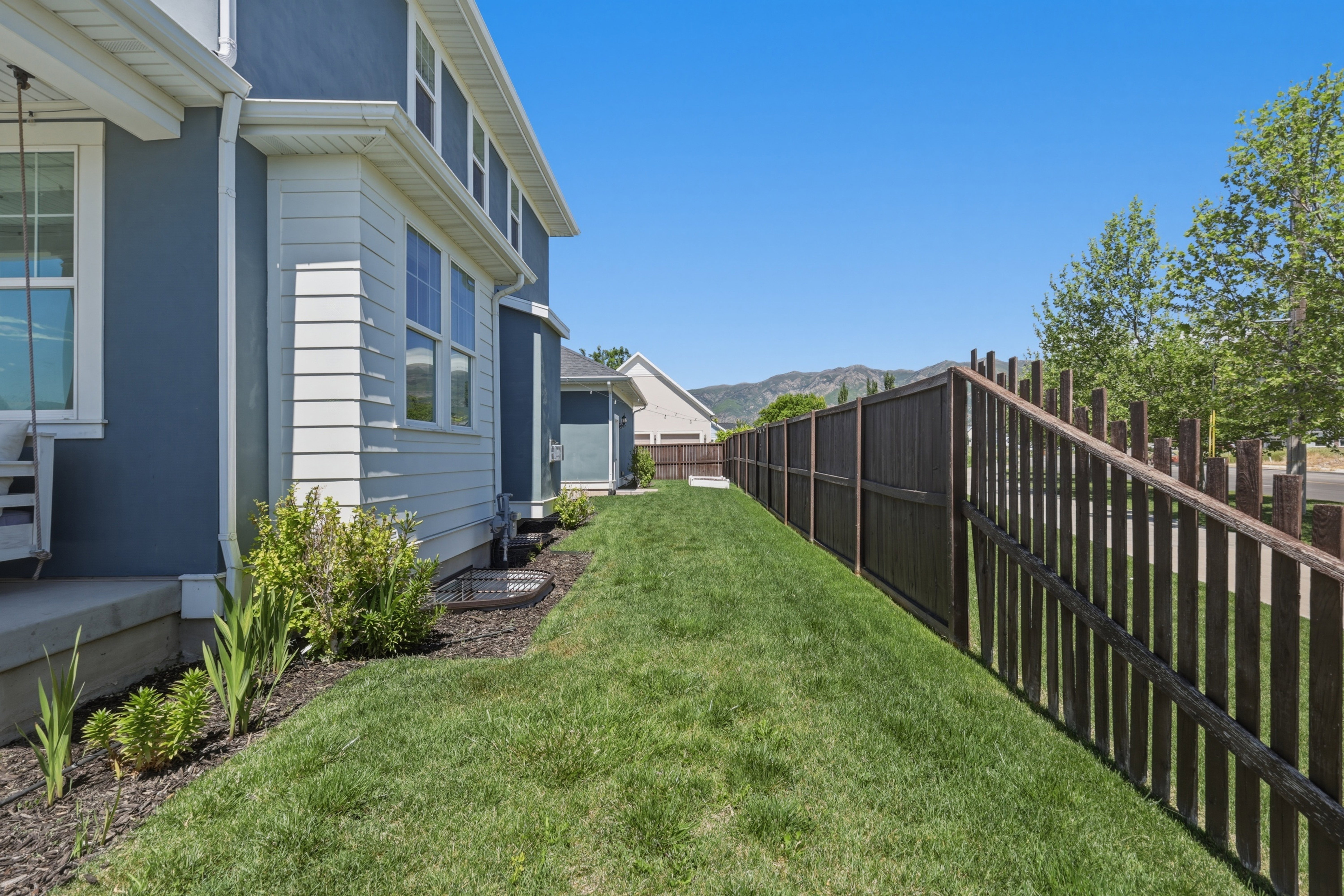 Side yard featuring a dark stained wood fence, manicured lawn, and mature landscaping