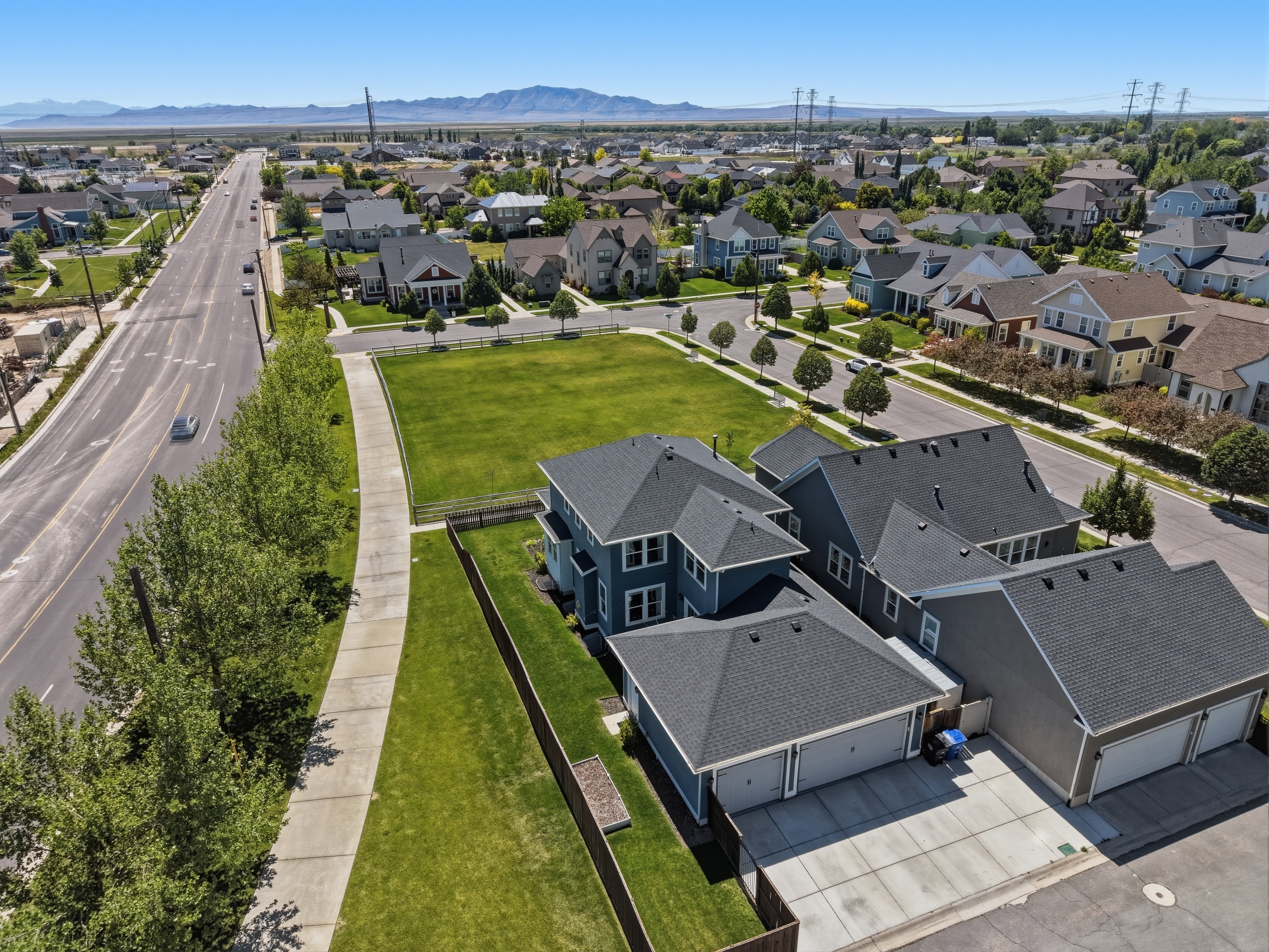 Aerial perspective showcasing a residential area with a paved road, manicured green spaces, and a distant mountain range