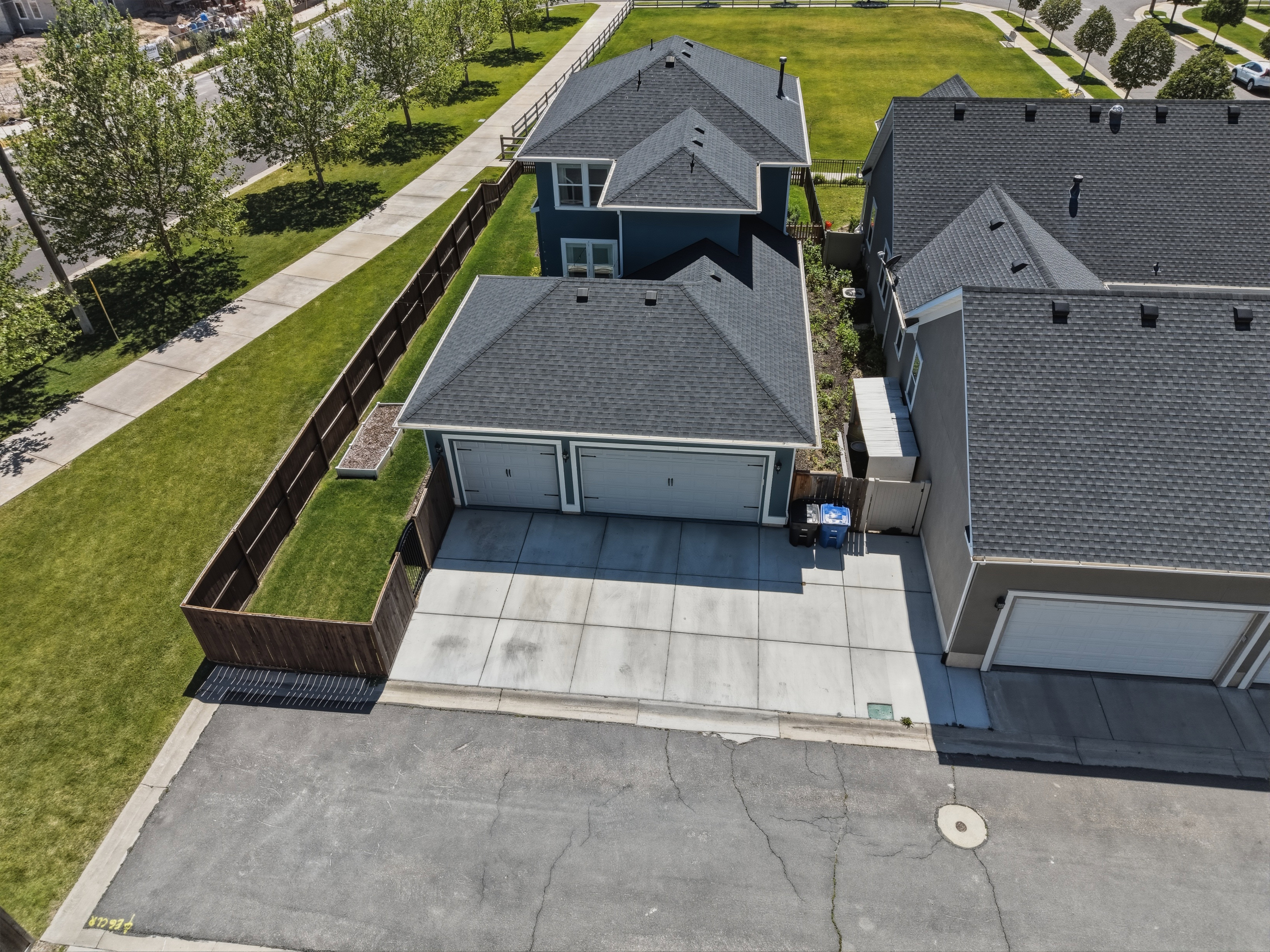 Two-story residential structure with a dark blue exterior, featuring a dual-bay garage with a concrete driveway, a private fenced yard, and shingled roofing