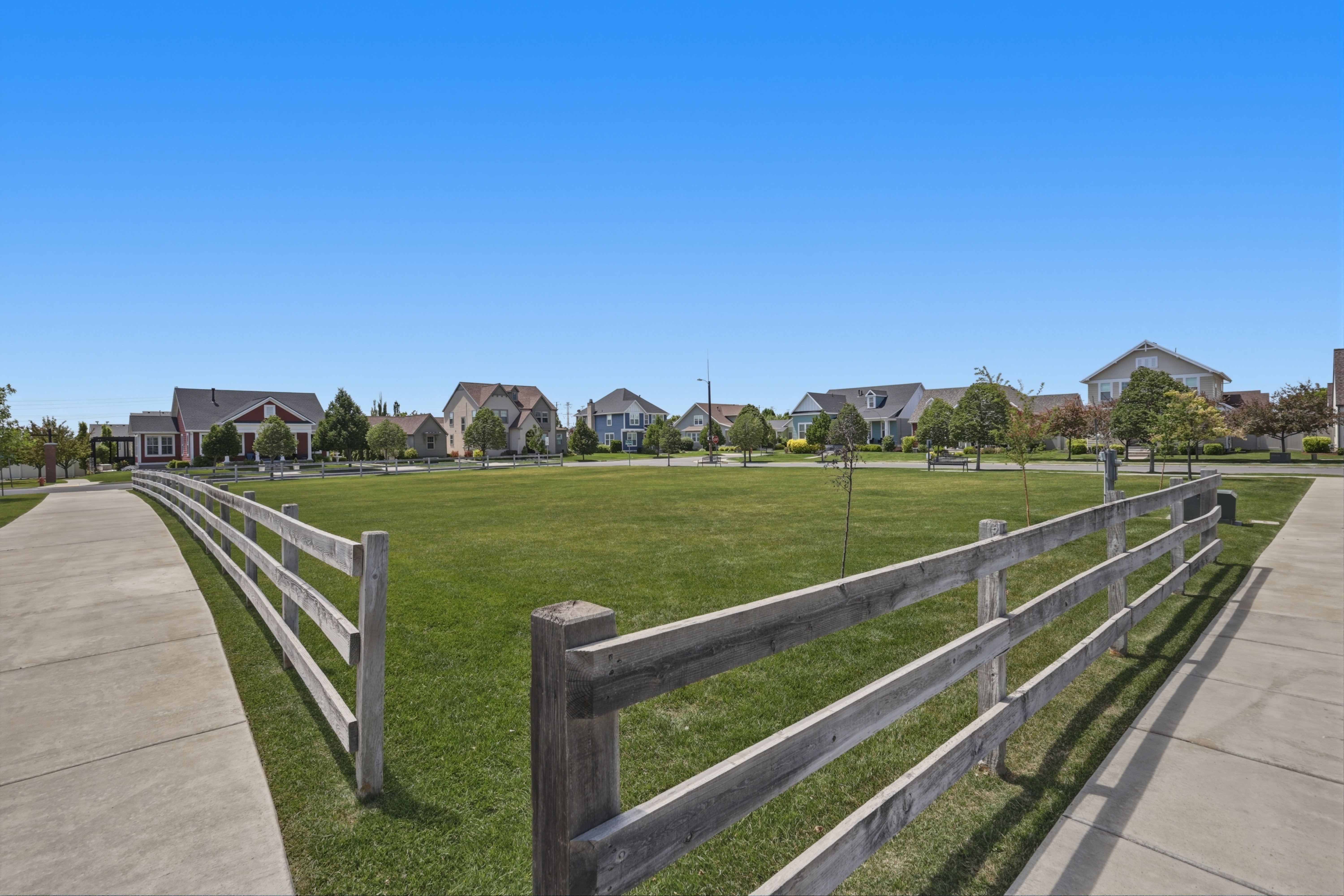 Expansive green space bordered by a rustic wooden fence and concrete pathways