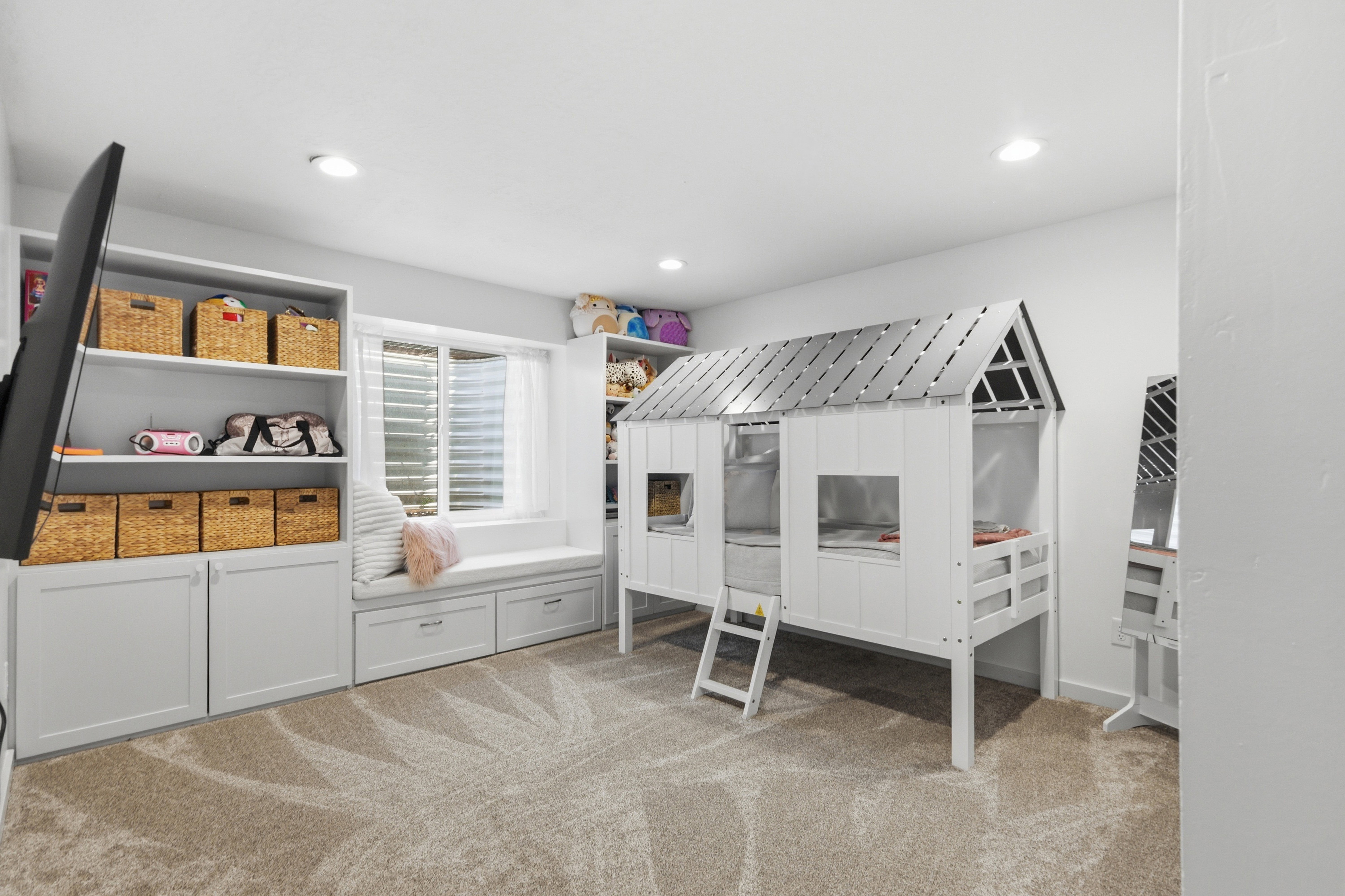 Recessed lighting illuminates a spacious room featuring built-in shelving, a window with horizontal blinds, and a window seat with integrated storage drawers