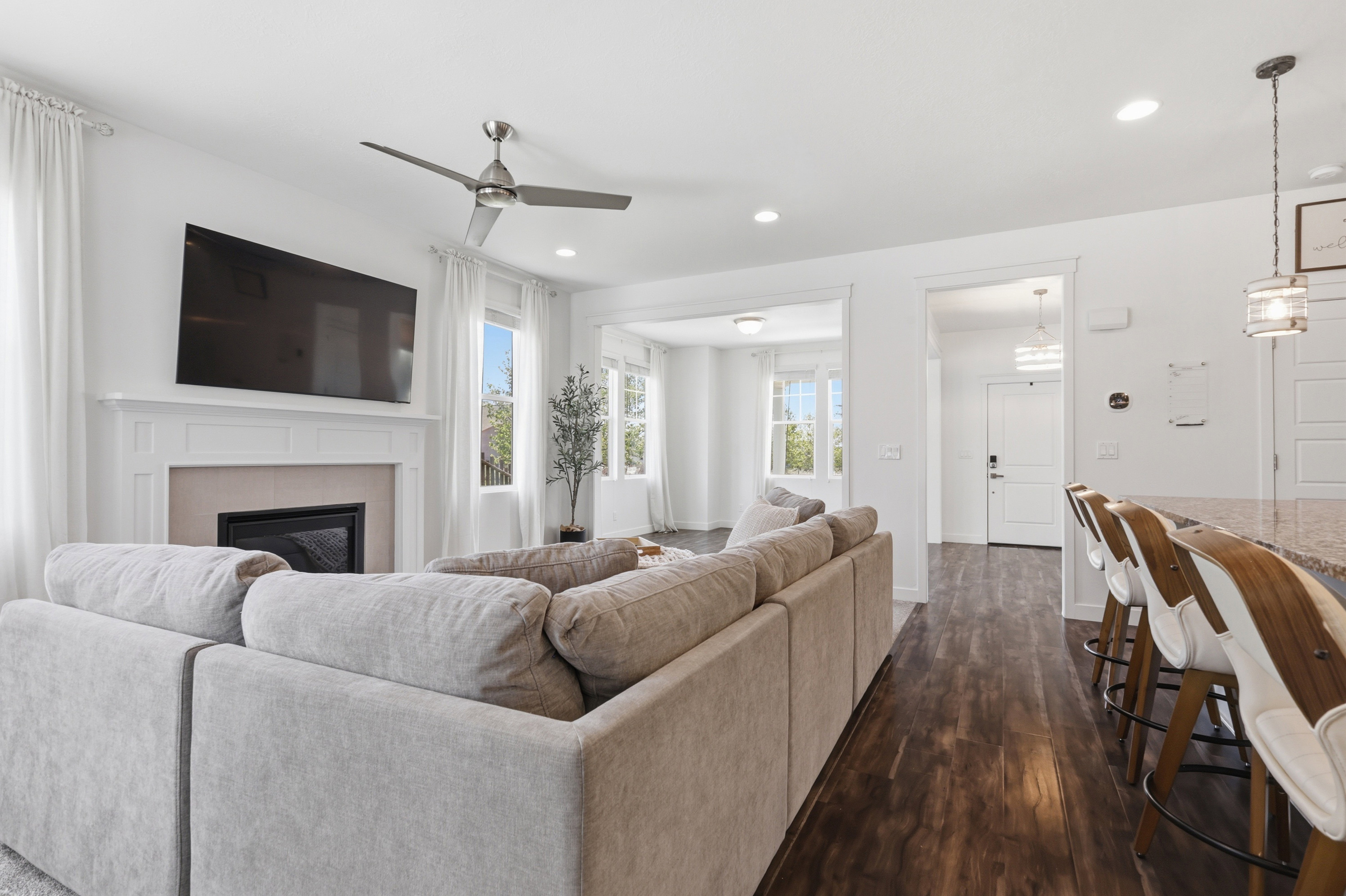 Open-concept living area with wood-finish flooring, a fireplace with a mantel, a ceiling fan, recessed lighting, and a breakfast bar with a stone countertop
