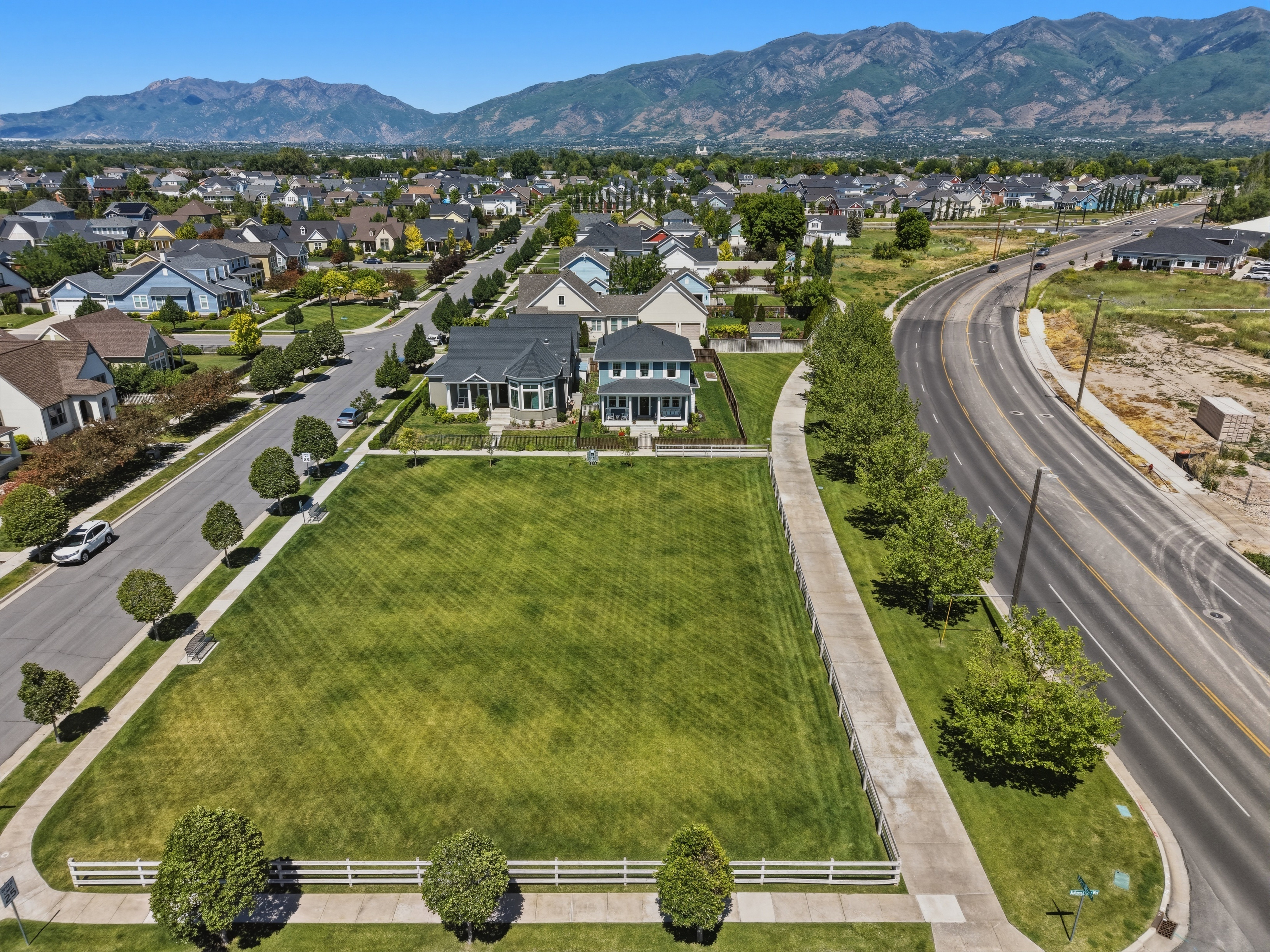 Expansive green space featuring a manicured lawn, white picket fencing, and mature trees