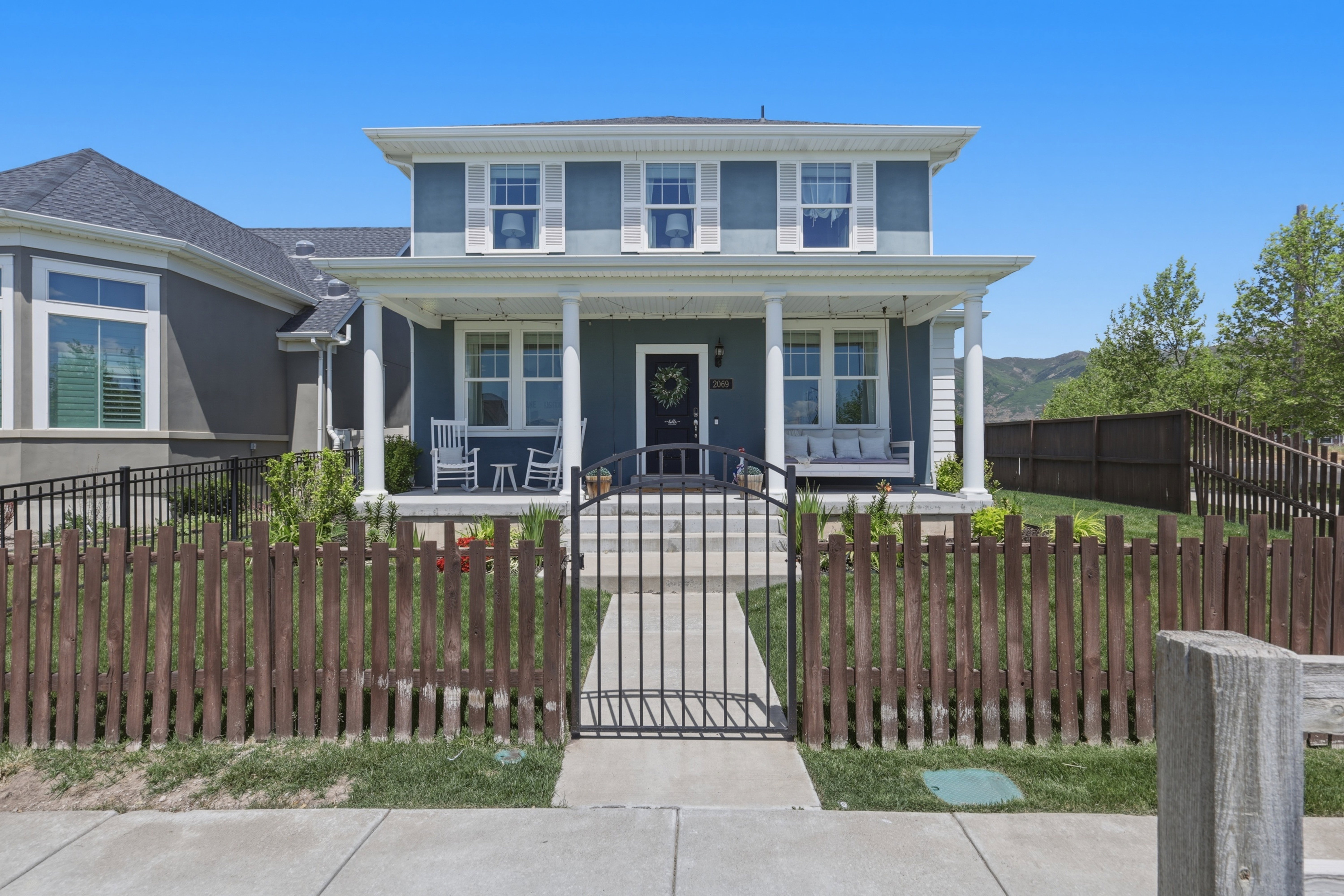 Two-story residence featuring a covered front porch with white pillars, white window shutters, and a black wrought iron gate