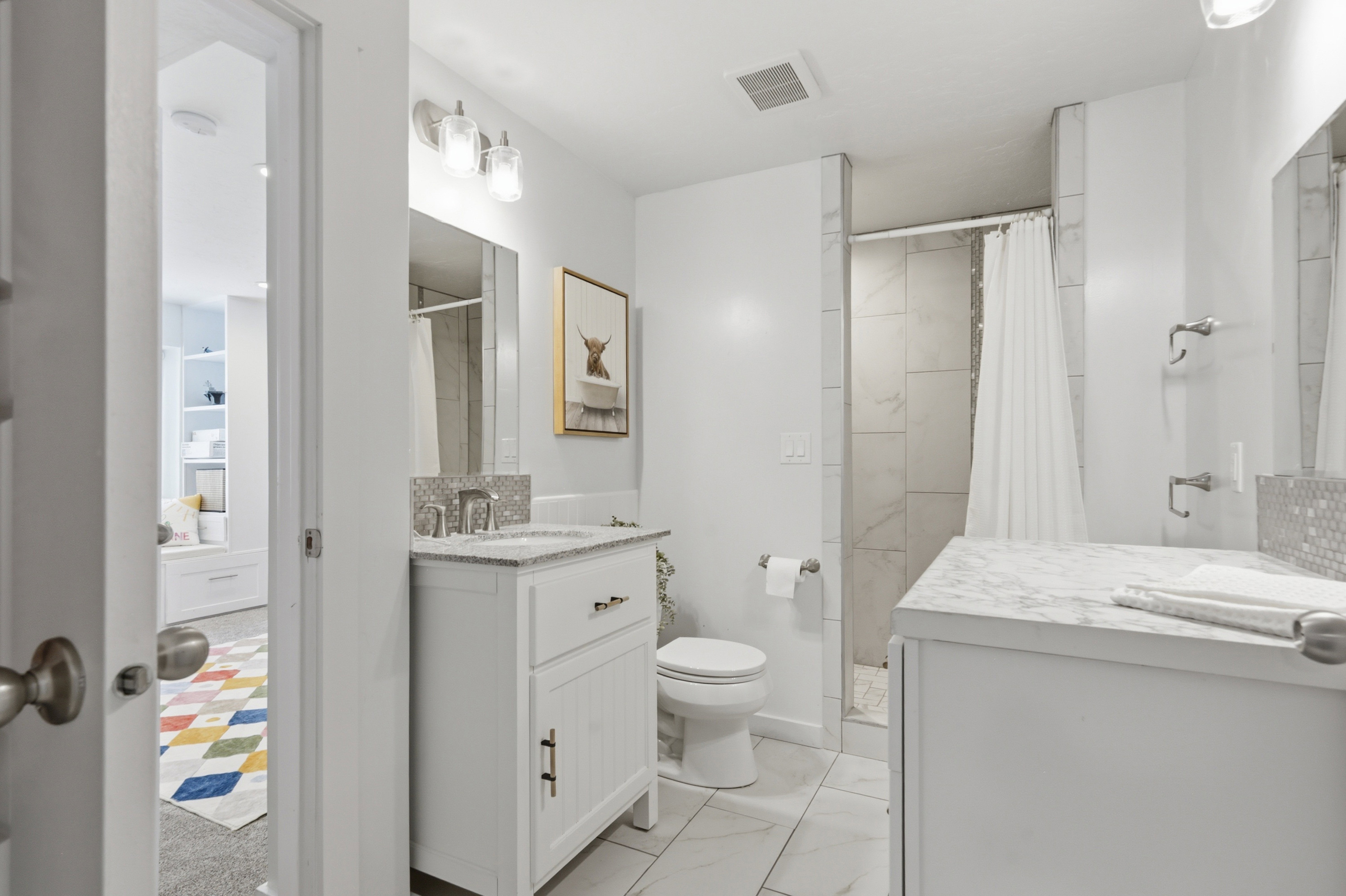 Full bathroom featuring dual white vanities with undermount sinks, stone countertops, and mosaic tile backsplashes