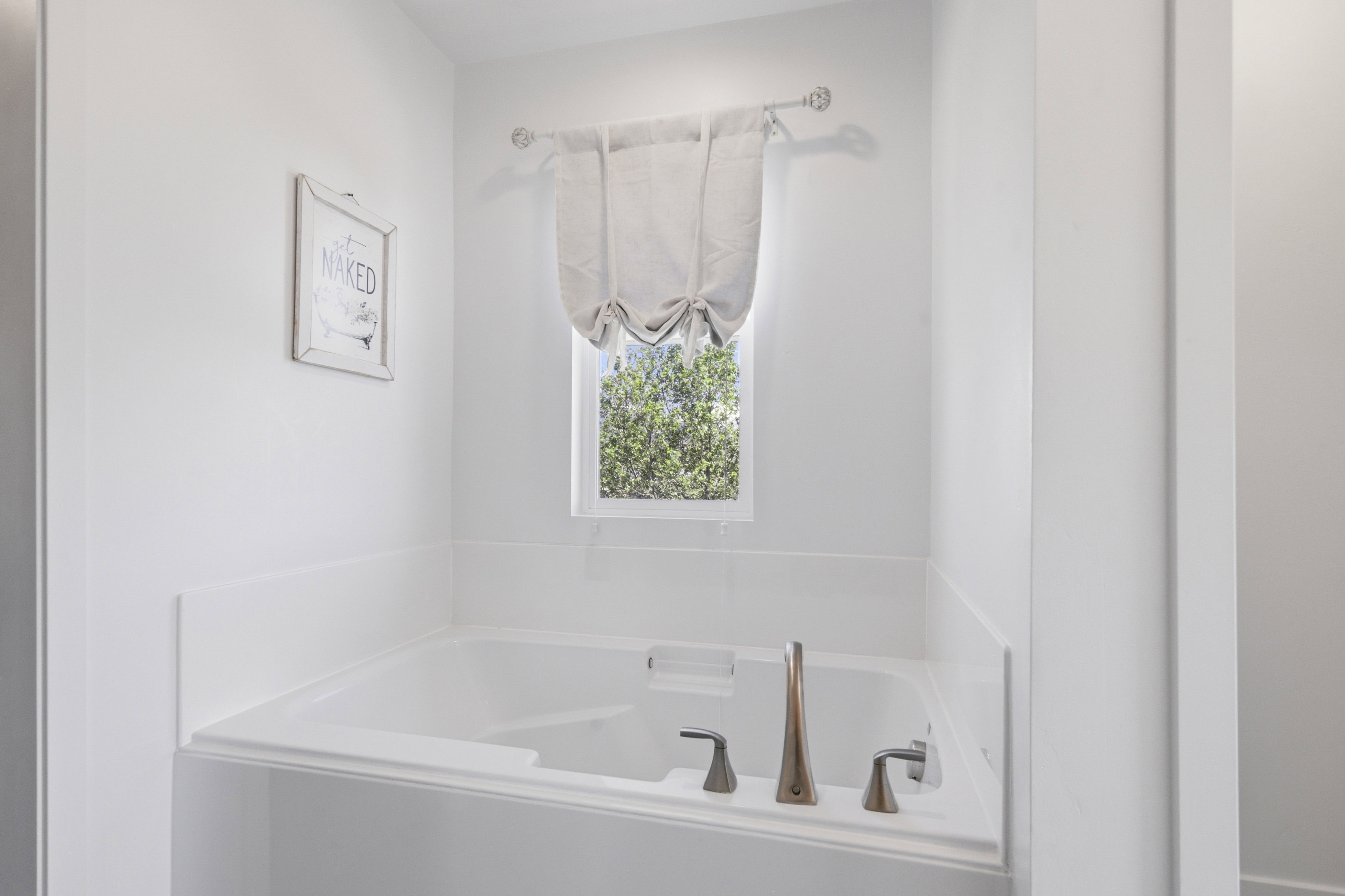 Built-in soaking tub featuring bronze-tone fixtures and a window with a fabric valence