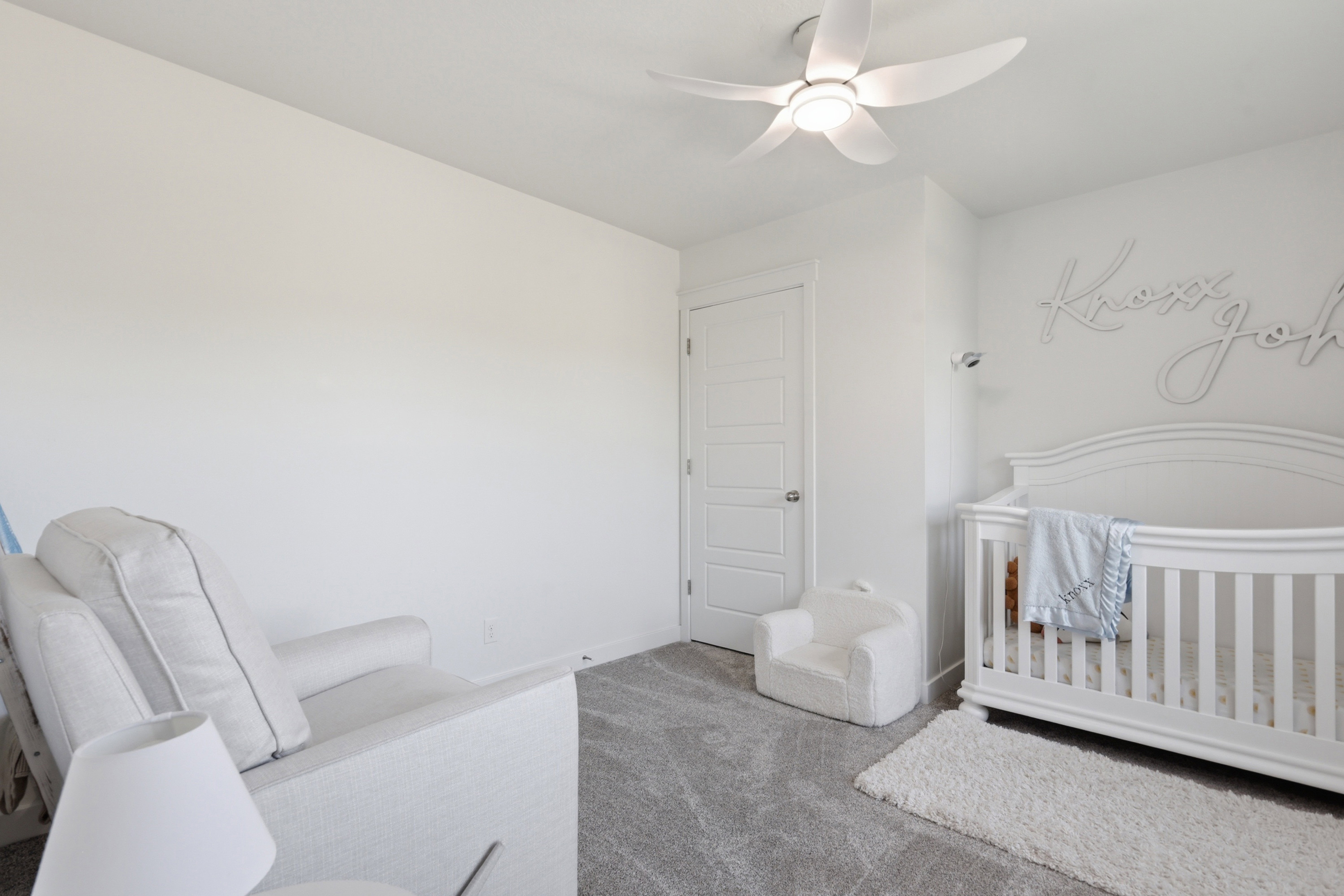 Bright interior room featuring a modern ceiling fan, white paneled door, and plush gray carpeting