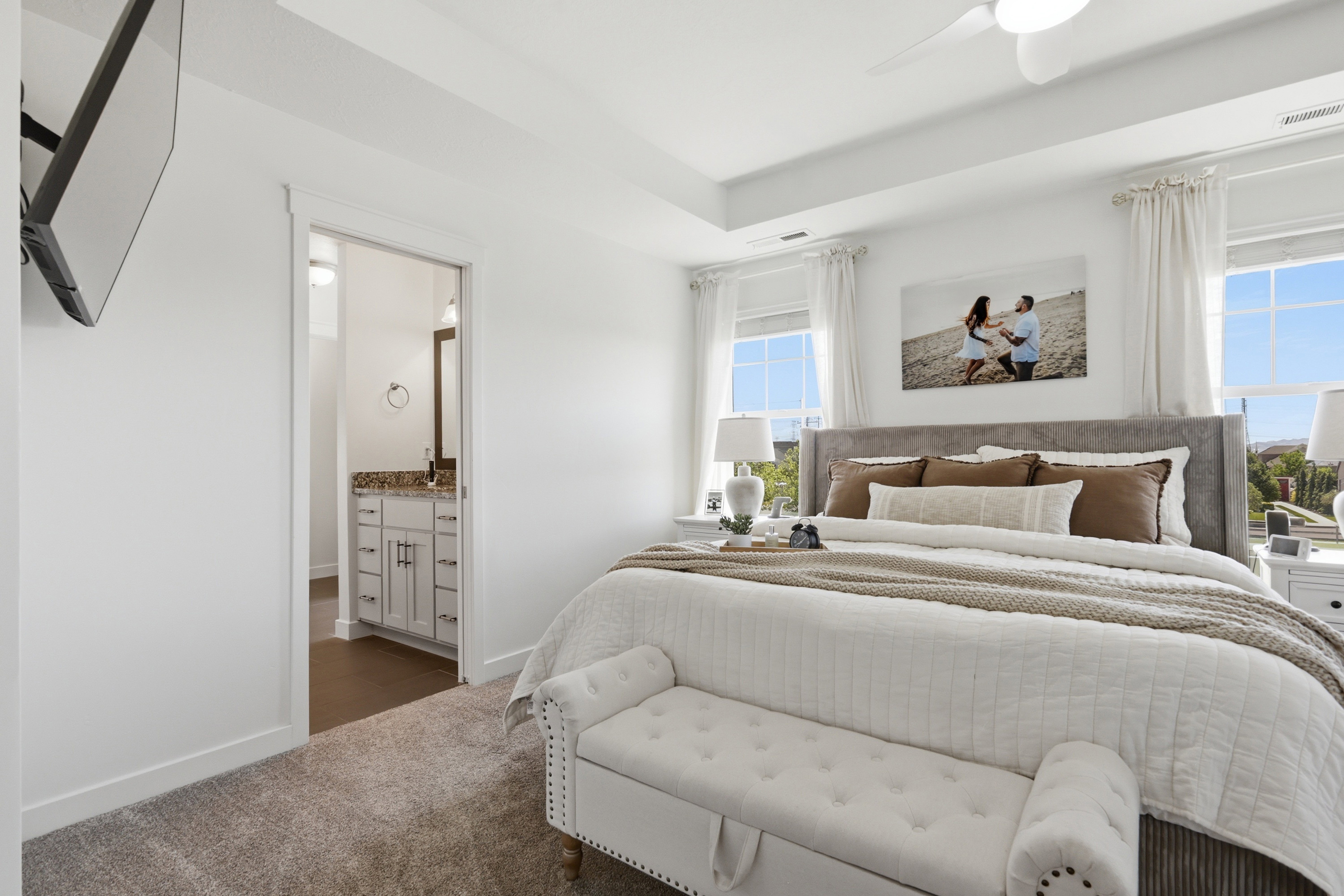 Recessed tray ceiling with a built-in ceiling fan, light gray carpeting, and two large windows