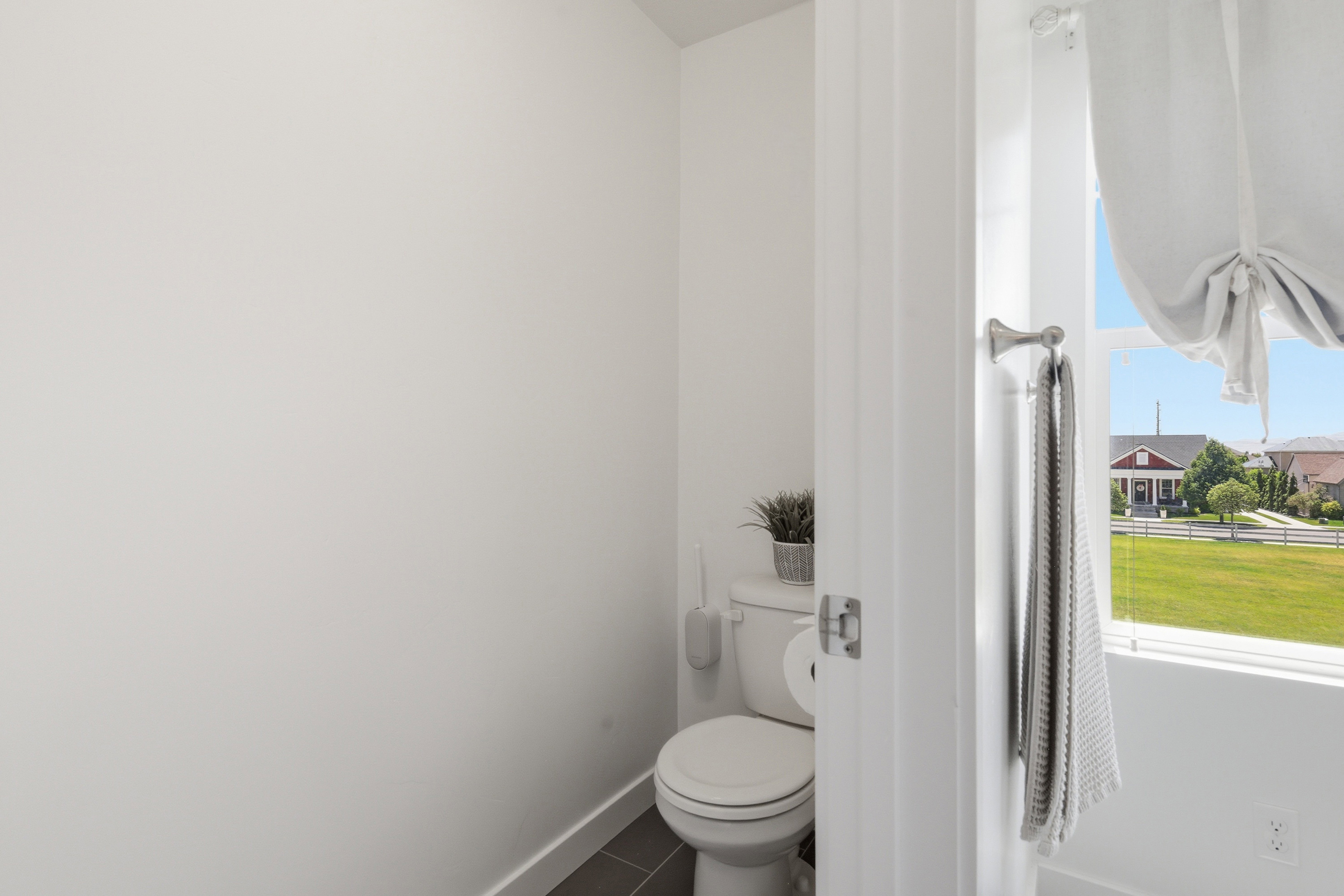 Compact bathroom featuring a white toilet, dark grey floor tiles, and a window with a fabric shade