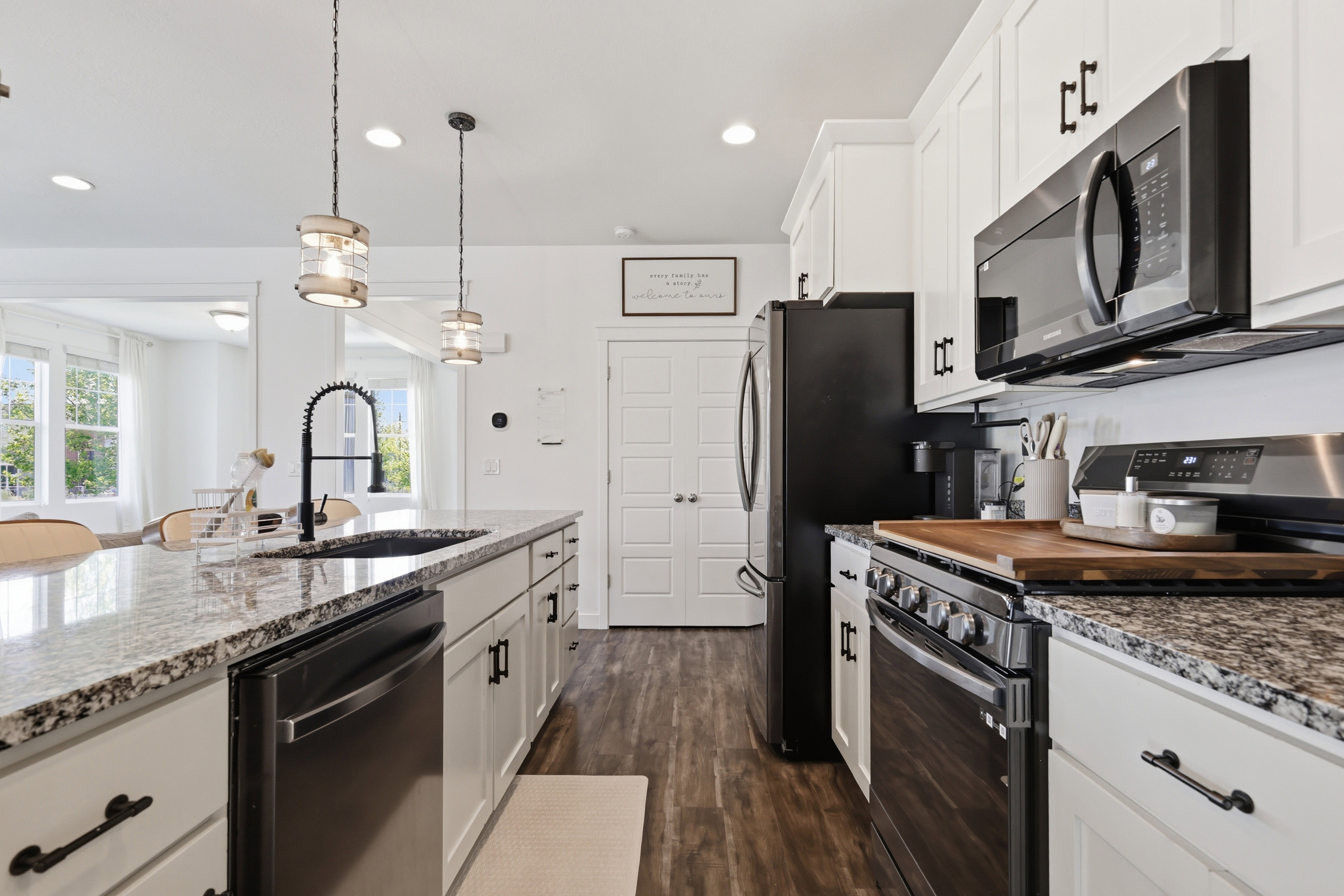 Modern kitchen featuring white cabinetry with dark hardware, a large kitchen island with granite countertops, and stainless steel appliances